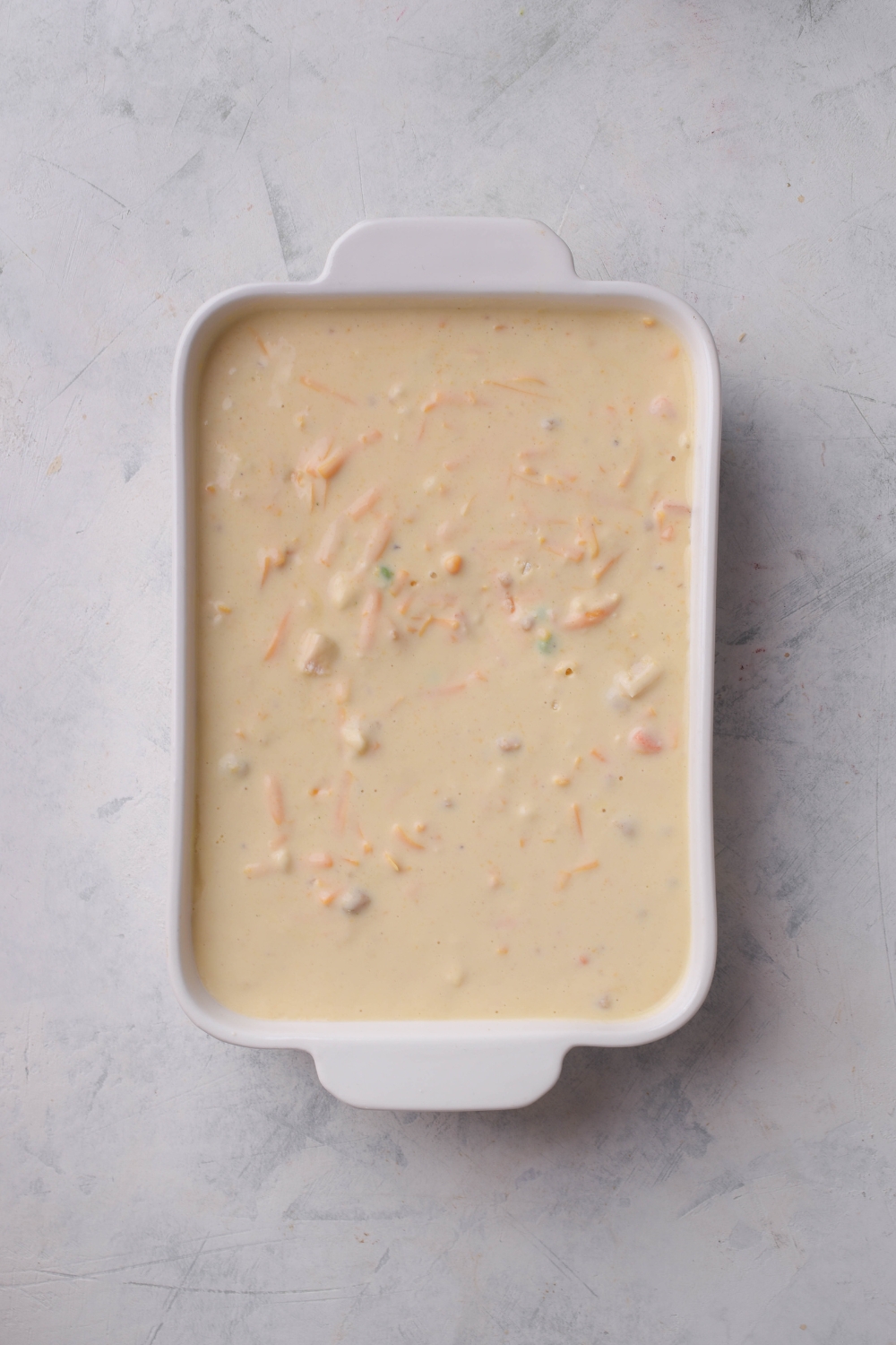 A baking dish filled with a creamy soup mixture and pieces of carrots and peas are visible.