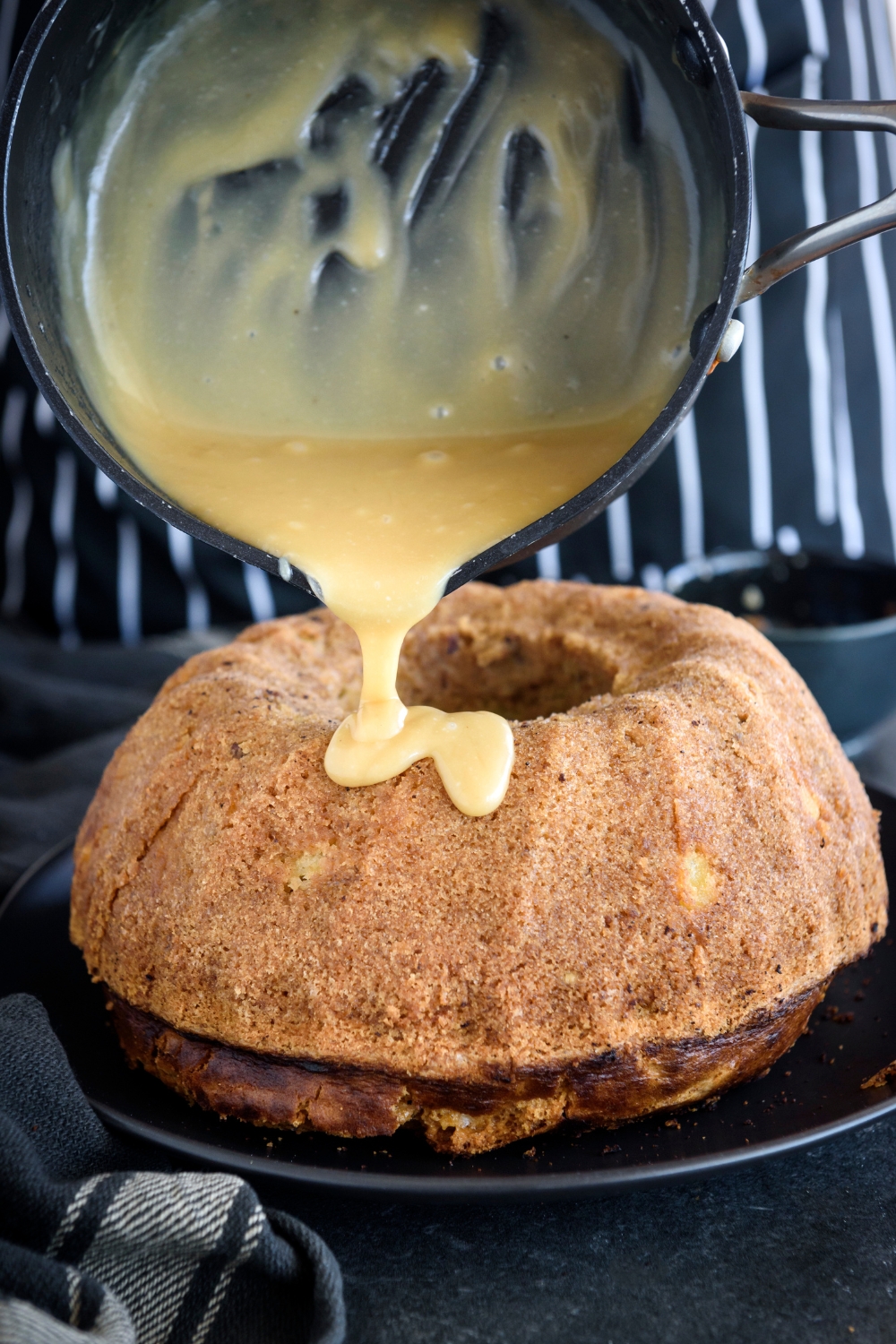 A pot of caramel sauce being drizzled over a bundt cake.