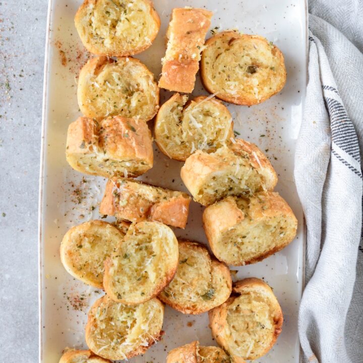 A plate filled with baguette garlic bread slices covered in seasonings.