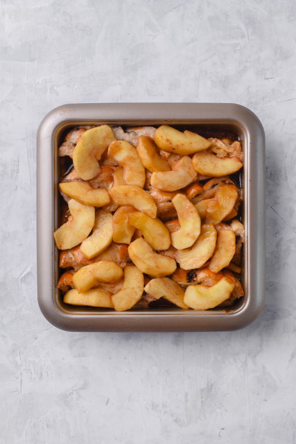 A square baking dish filled with bread slices topped with stewed apples covered in cinnamon.