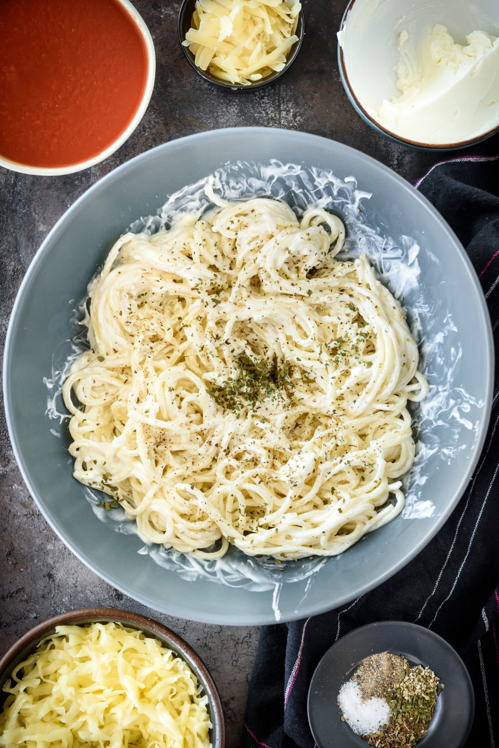 A bowl filled with cooked spaghetti noodles covered in a creamy sauce with a pile of seasonings in the center of the spaghetti.