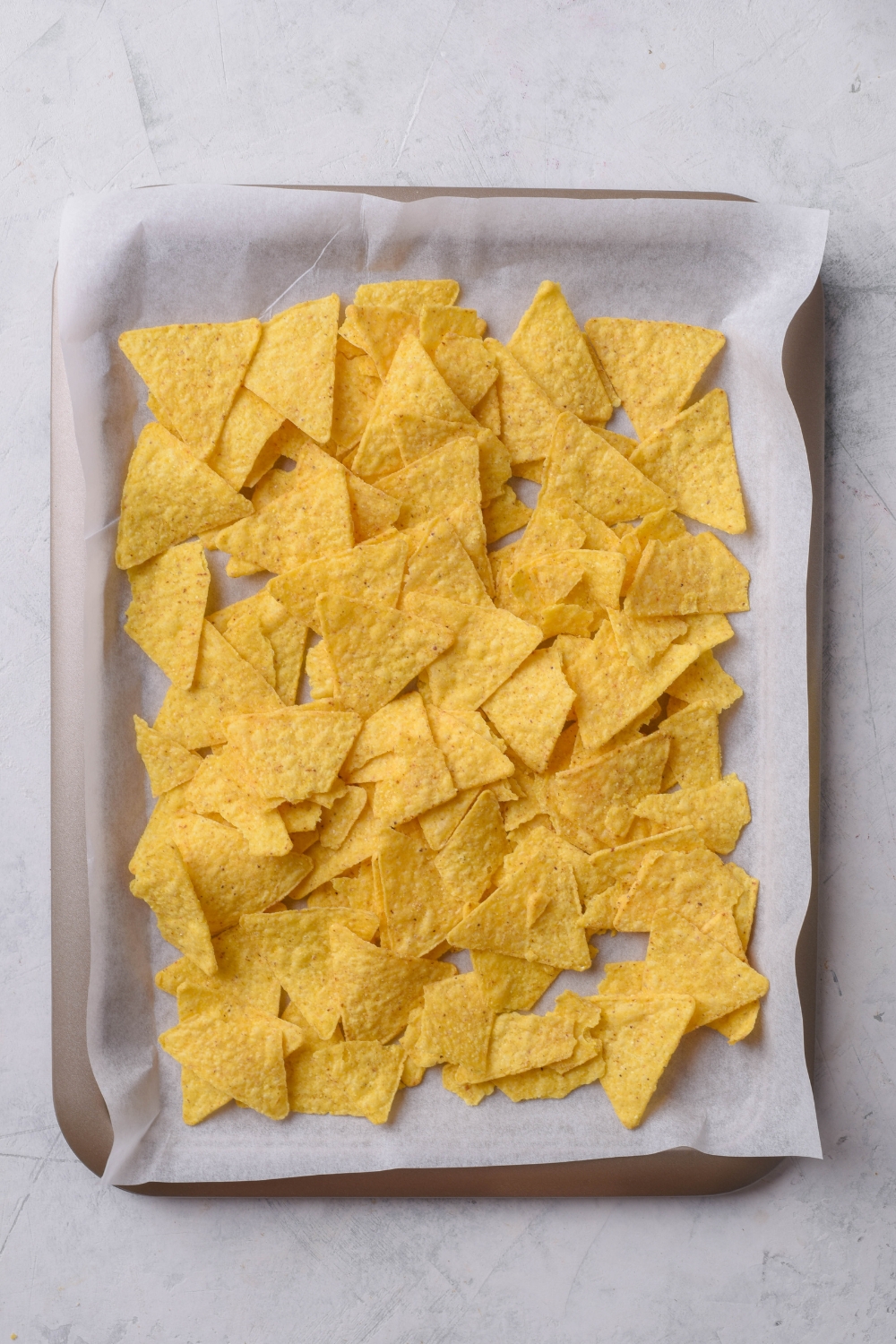A baking sheet lined with parchment paper covered in a layer of tortilla chips.