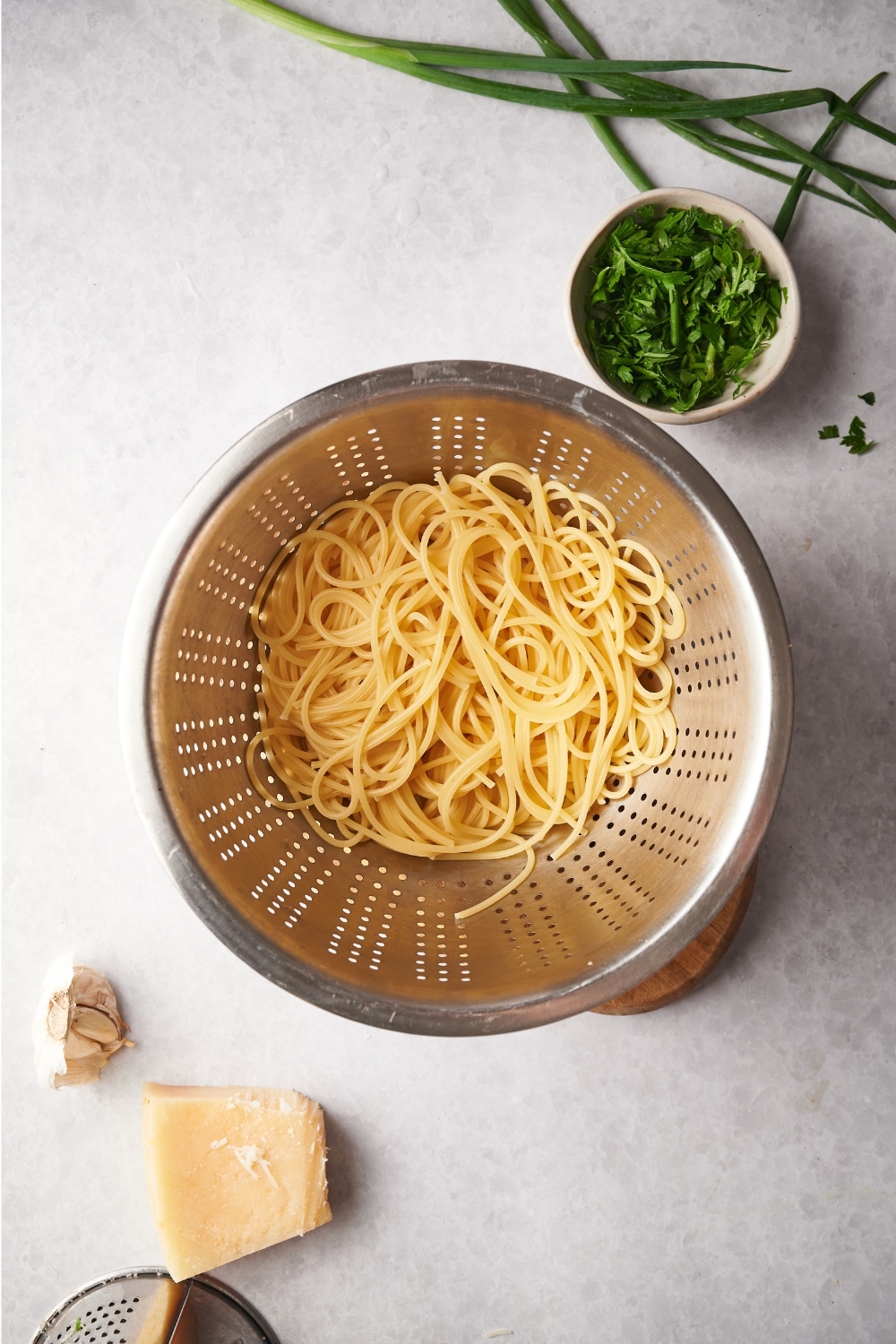 A colander filled with cooked spaghetti noodles surrounded by an assortment of ingredients.