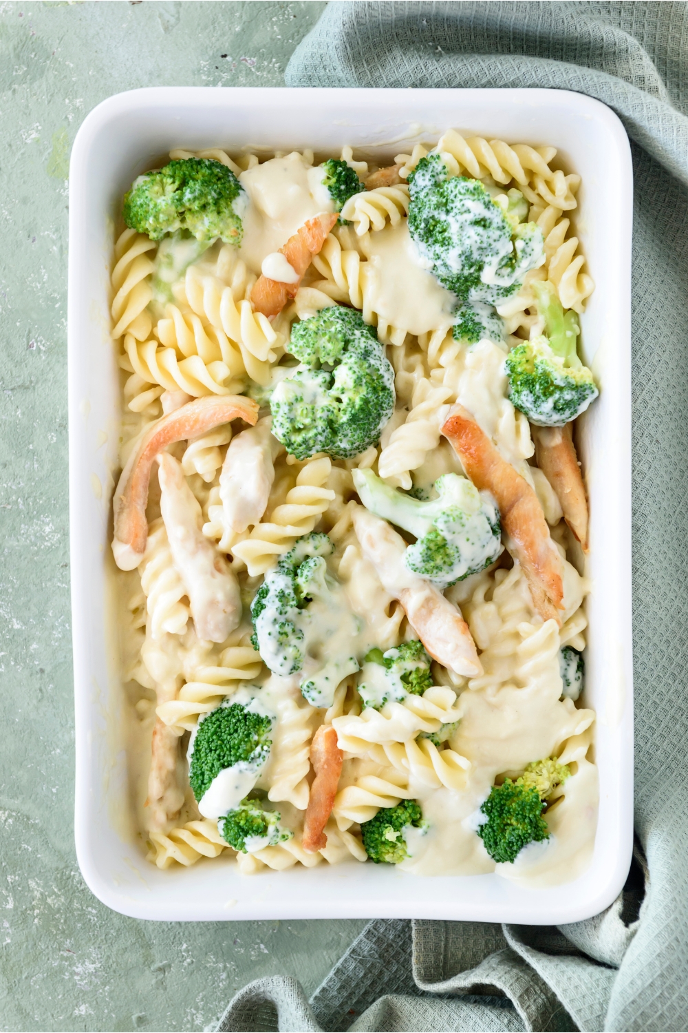 A baking dish filled with cooked pasta, broccoli, and chicken strips in a creamy sauce.