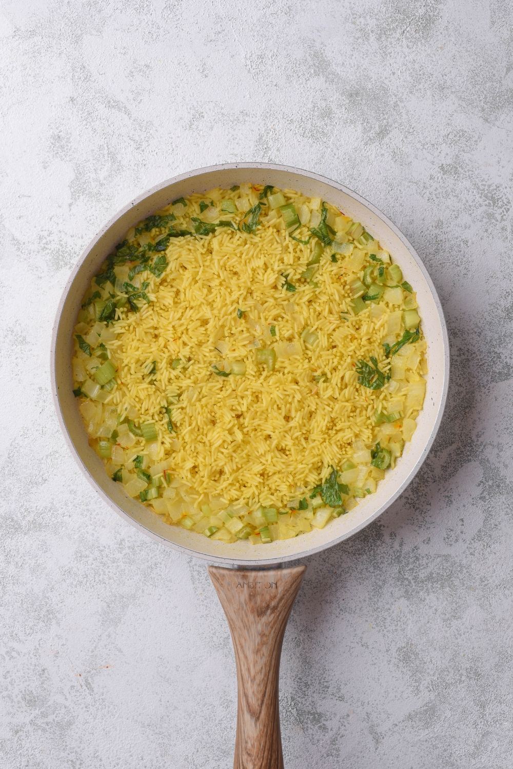 A skillet filled with yellow rice, fresh parsley, diced celery, and diced onion.