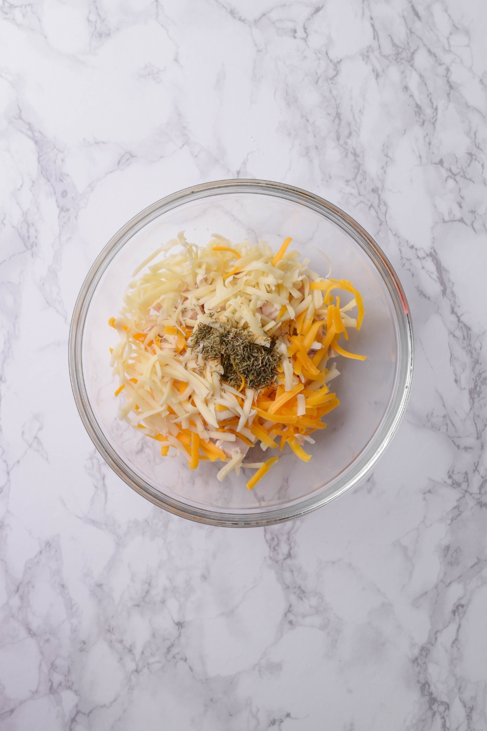 A clear bowl filled with shredded cheese and seasonings.
