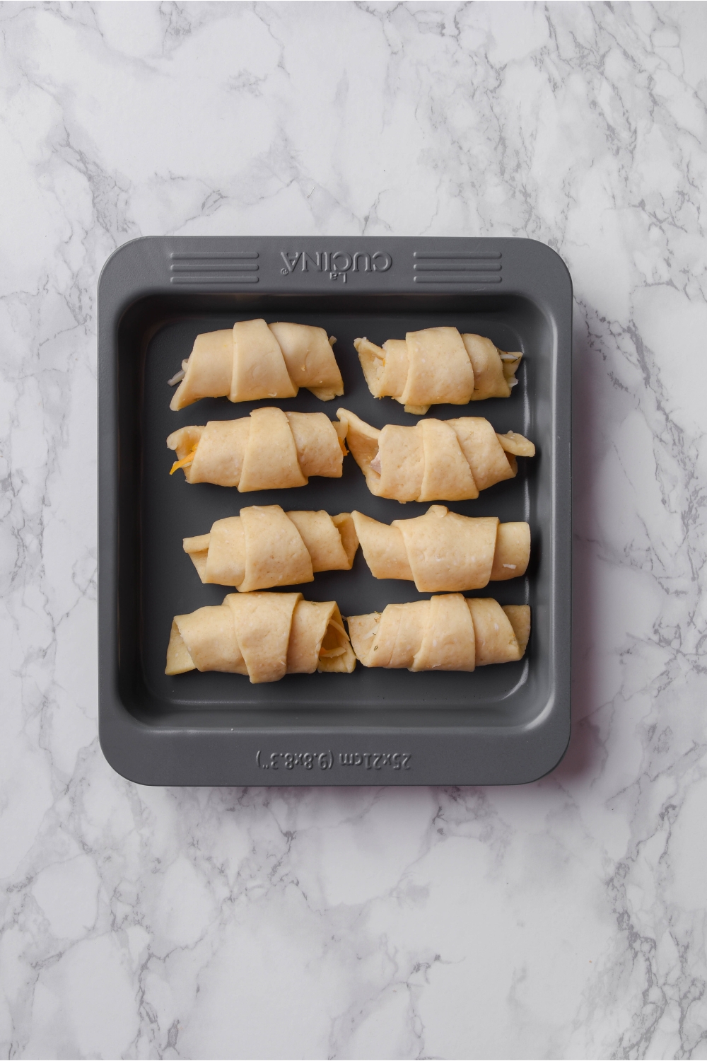 A square baking dish filled with eight unbaked crescent rolls.