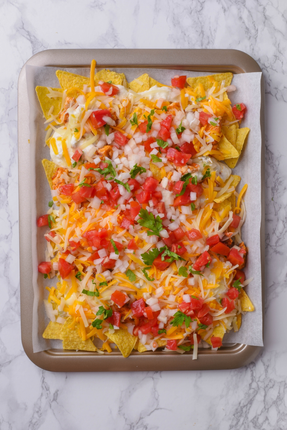 A baking sheet lined with parchment paper topped with tortilla chips, shredded cheese, and pico de gallo.