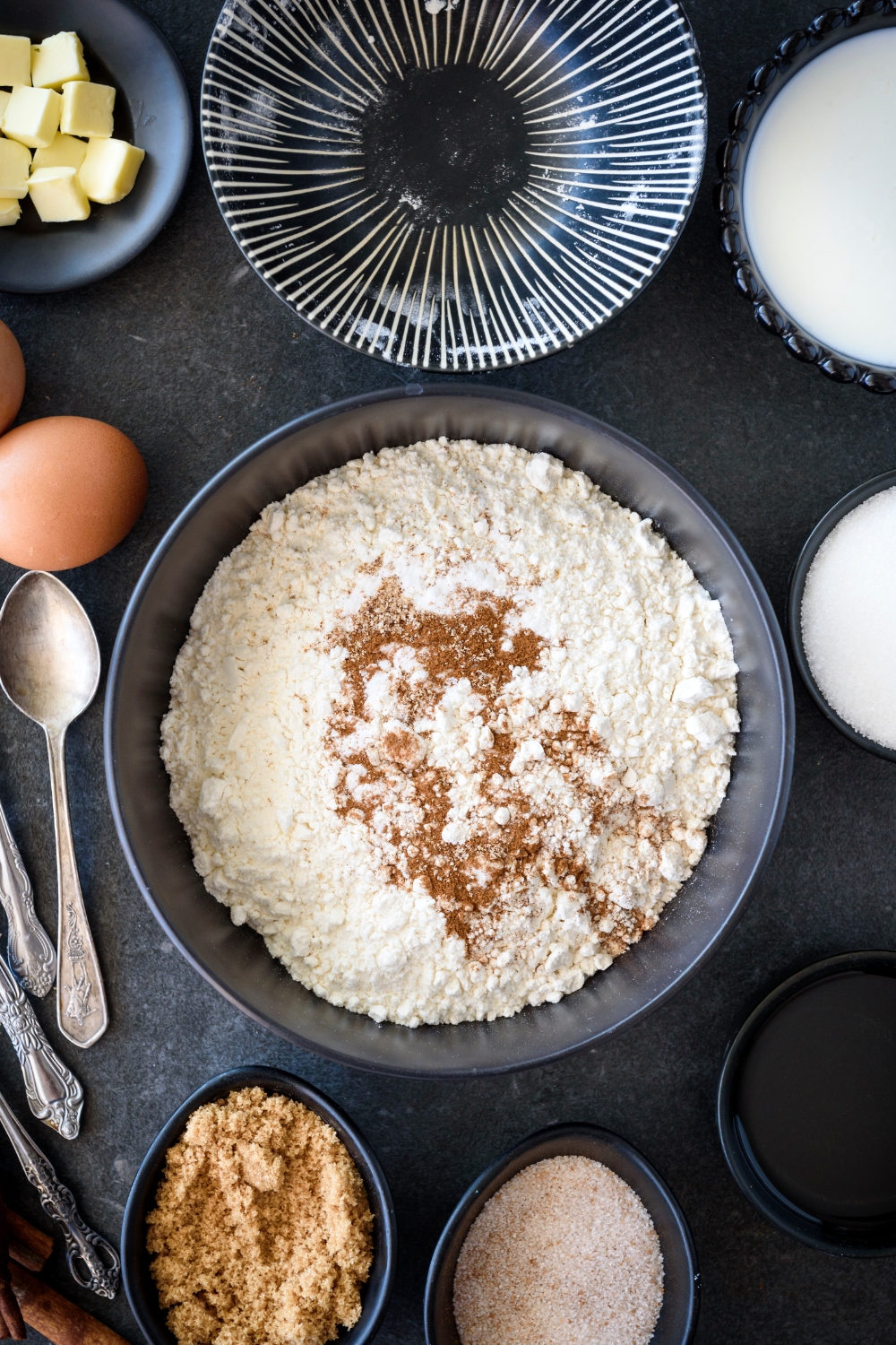 A bowl filled with flour and cinnamon surrounded by an assortment of ingredients.