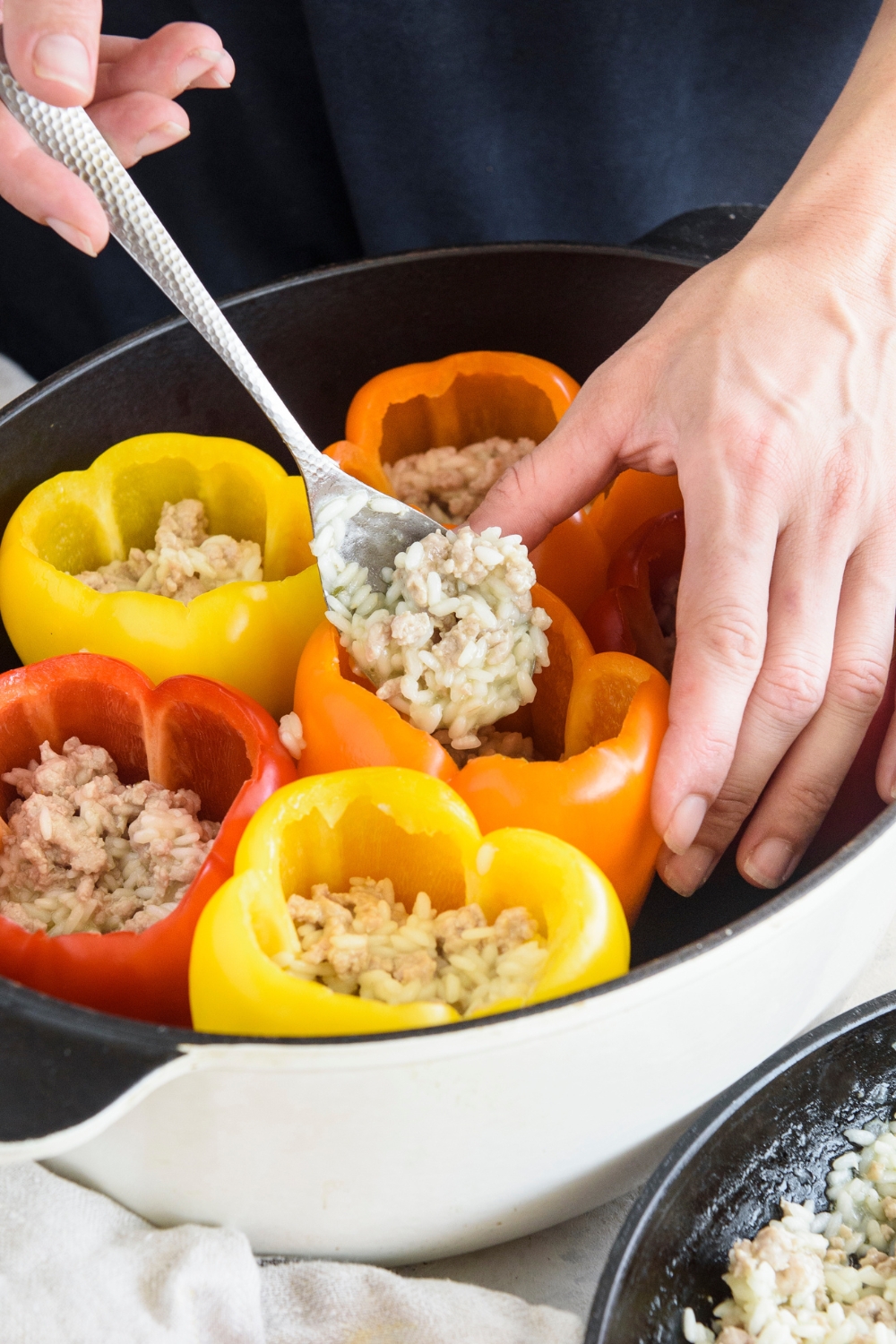 A person using a spoon to stuff bell peppers with a rice and ground meat mixture.