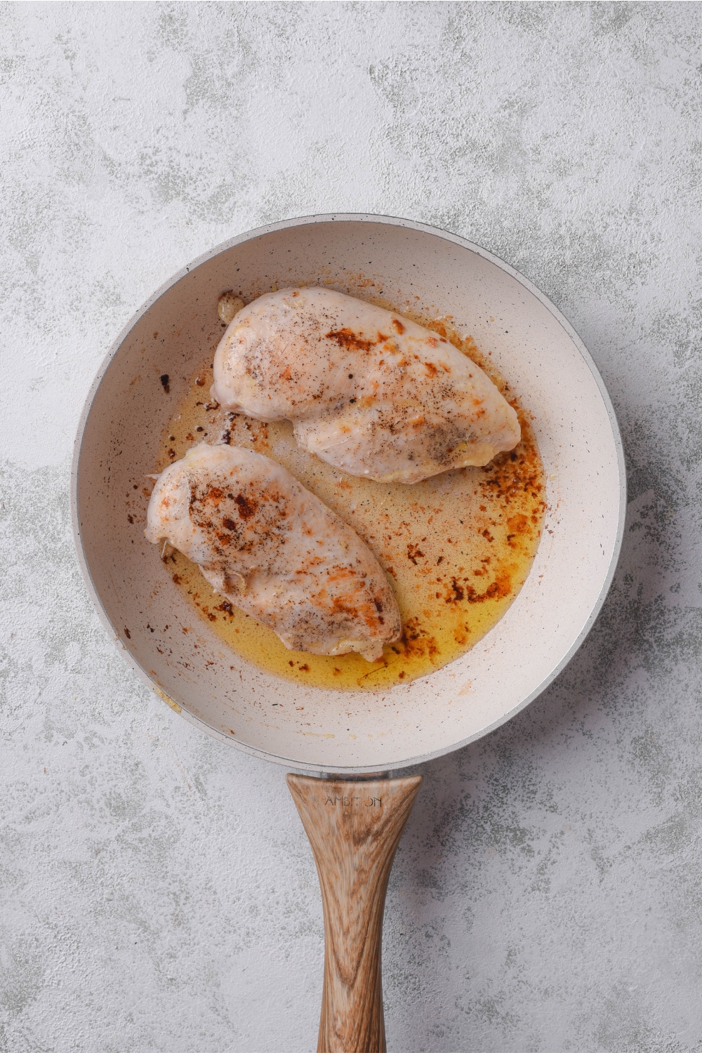 A skillet with two seasoned chicken breasts cooking in oil.