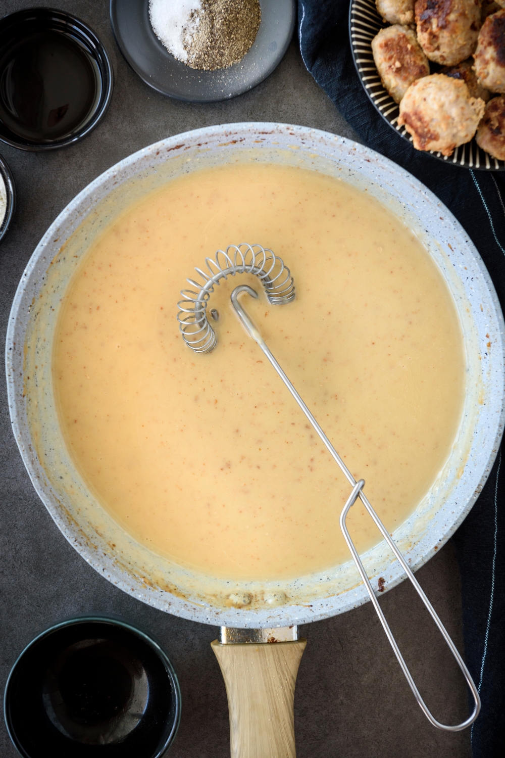 A skillet filled with a creamy sauce and a whisk is in the skillet.