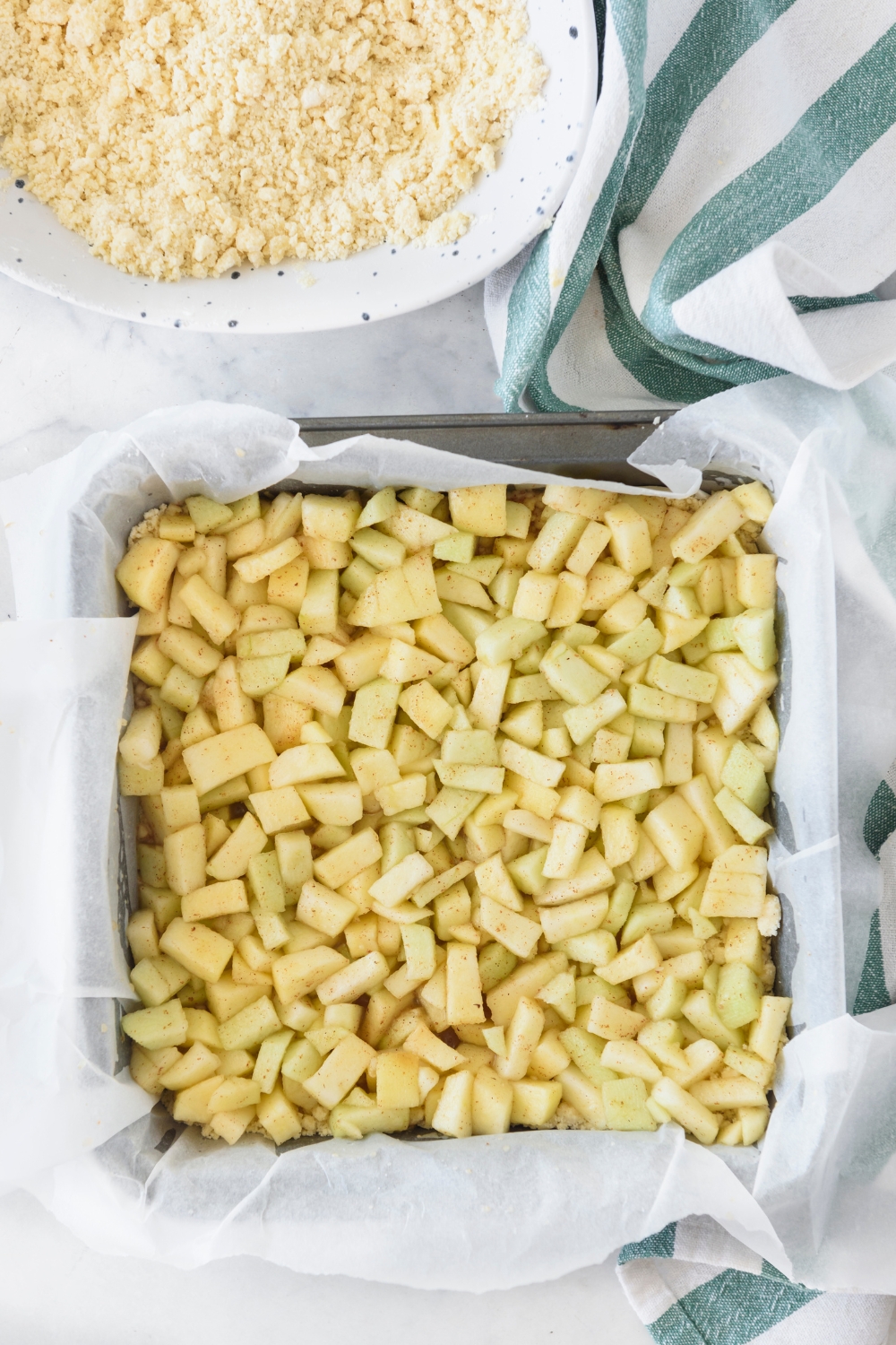 A square baking dish lined with parchment paper filled with diced apples.