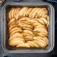 A square baking dish filled with freshly baked apple slices coated in cinnamon and sugar.