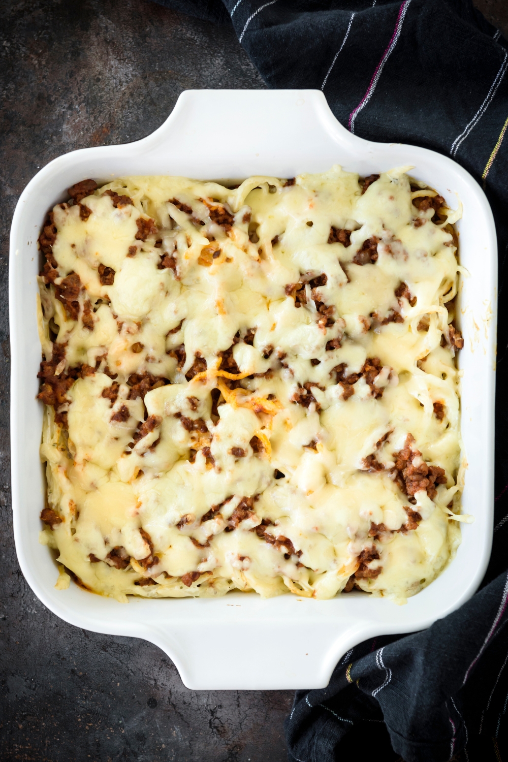 A baking dish filled with freshly baked spaghetti covered in melted cheese.