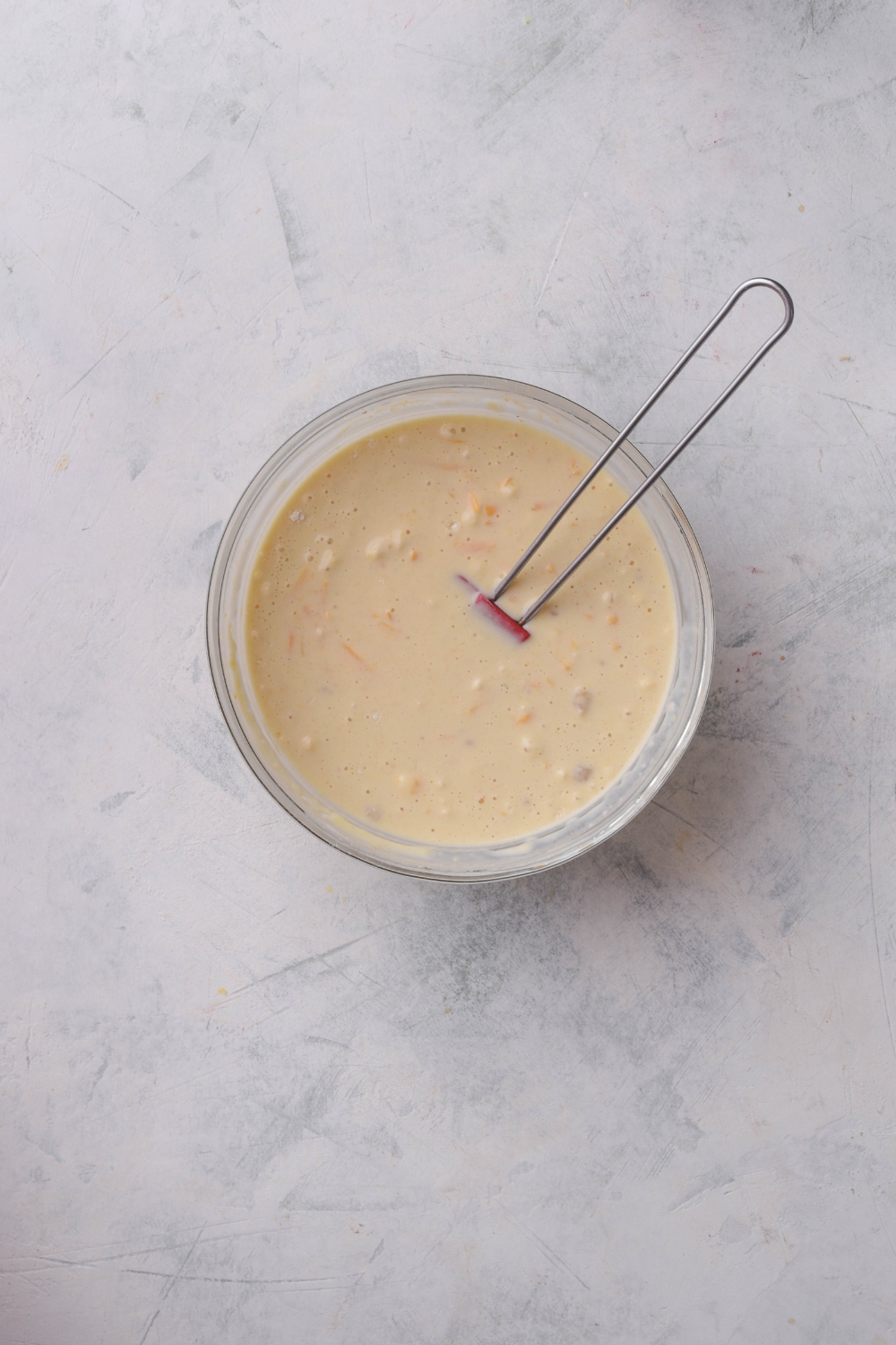 A clear bowl filled with creamy soup mixture and a kitchen utensil is in the bowl.