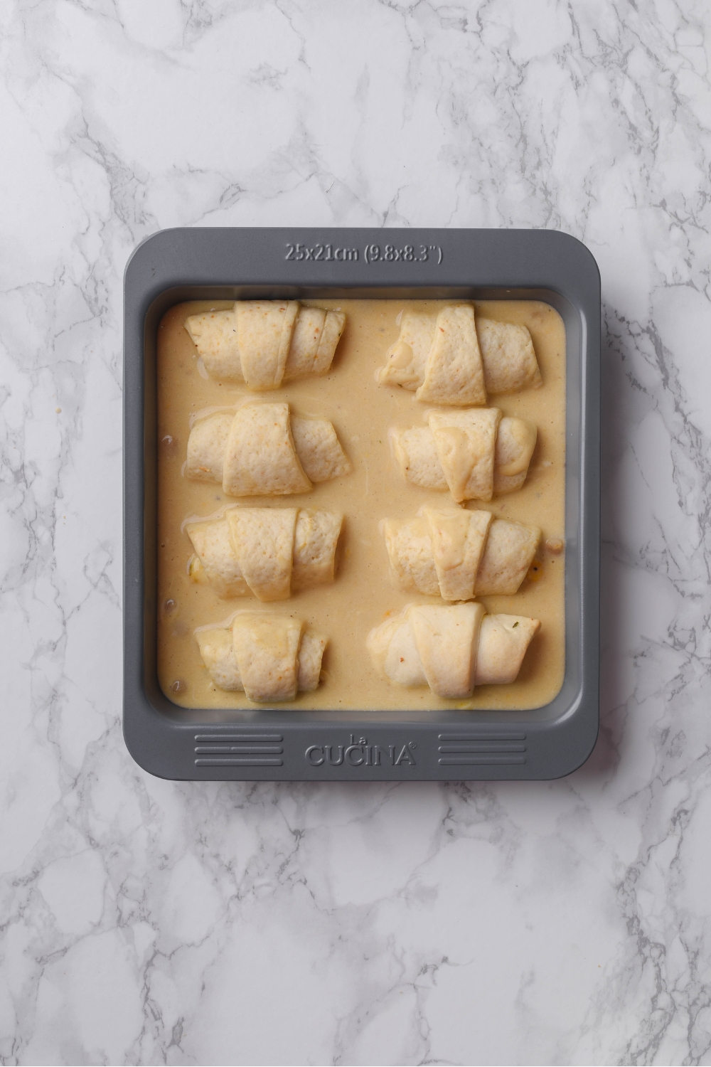 A square baking dish filled with eight freshly baked crescent rolls almost completely covered in cream sauce.