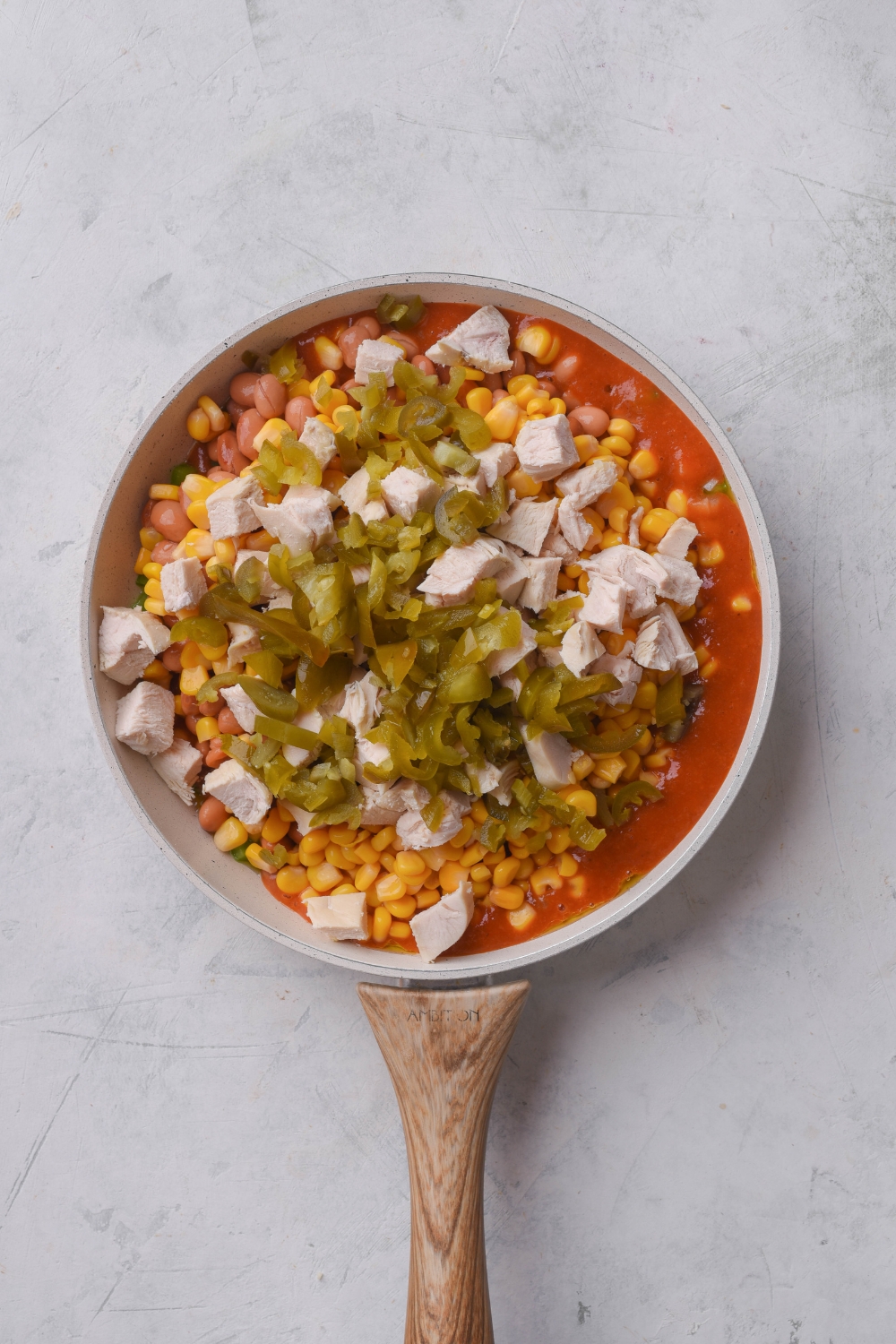 A skillet filled with cooked and diced chicken, corn, beans, peppers, onions, green chiles, and red sauce in it.