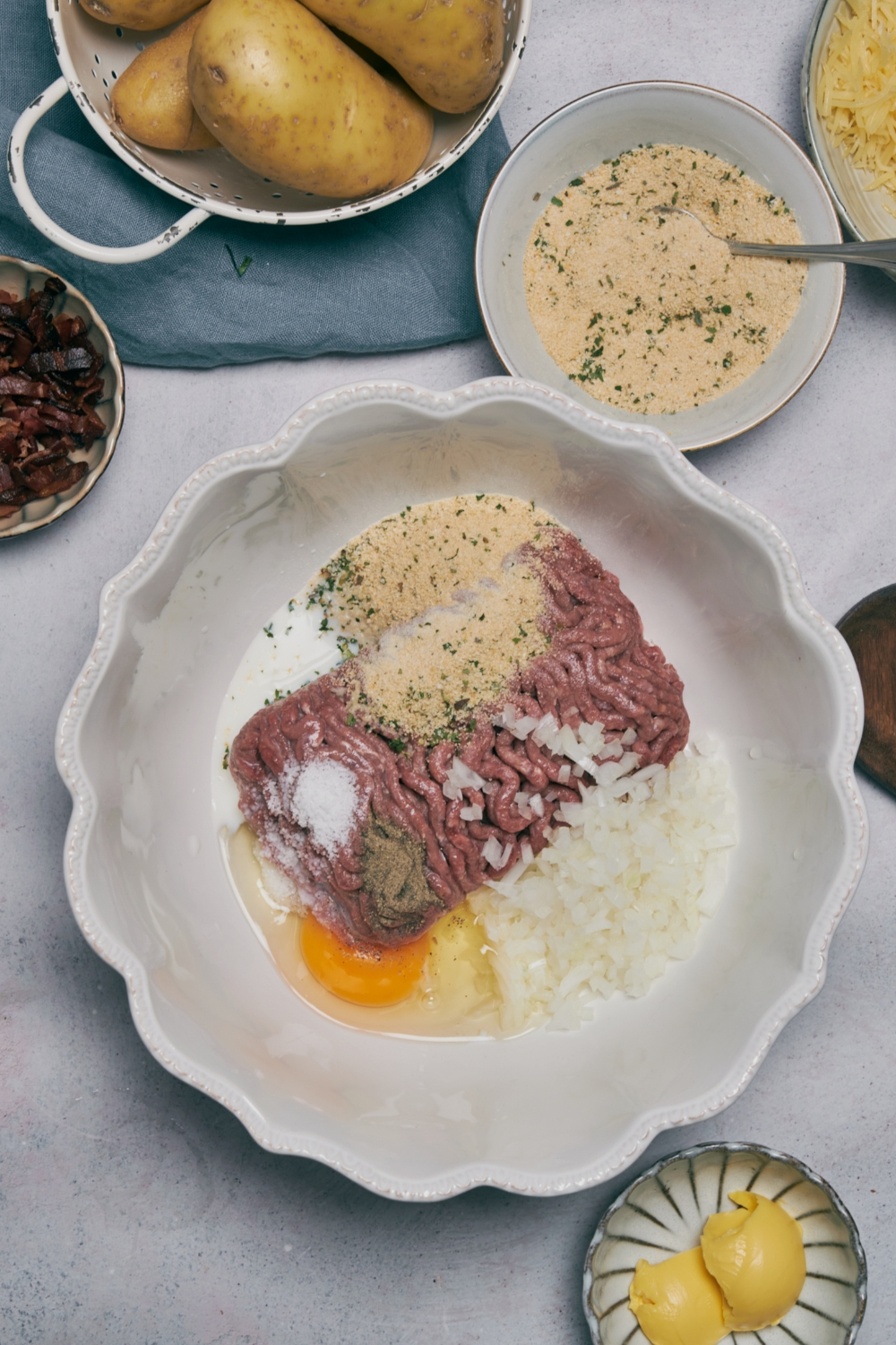 Ground meat, spices, a cracked egg, and onion in a white bowl.