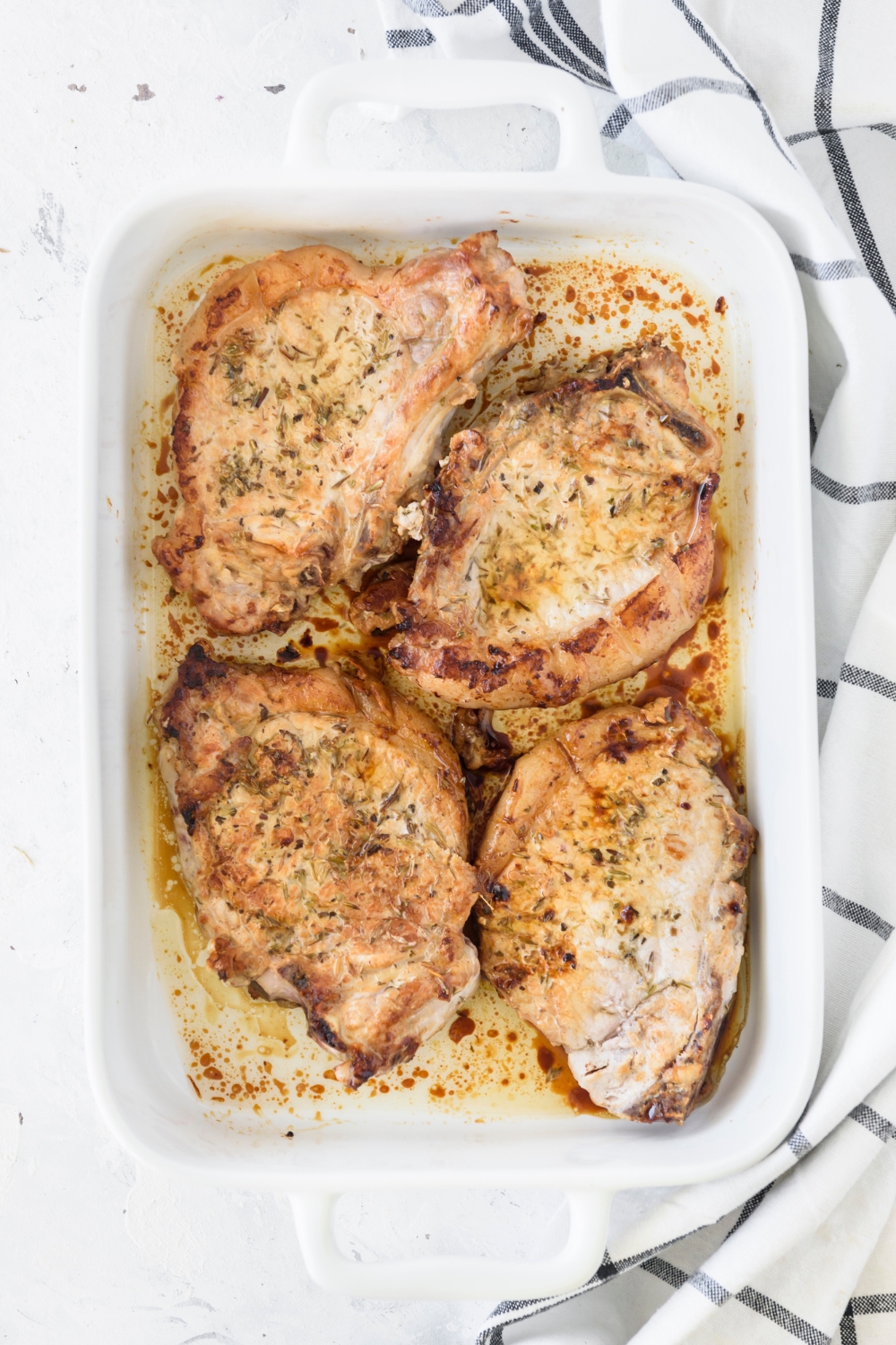 A baking dish filled with baked pork chops covered in seasonings in a cream sauce.