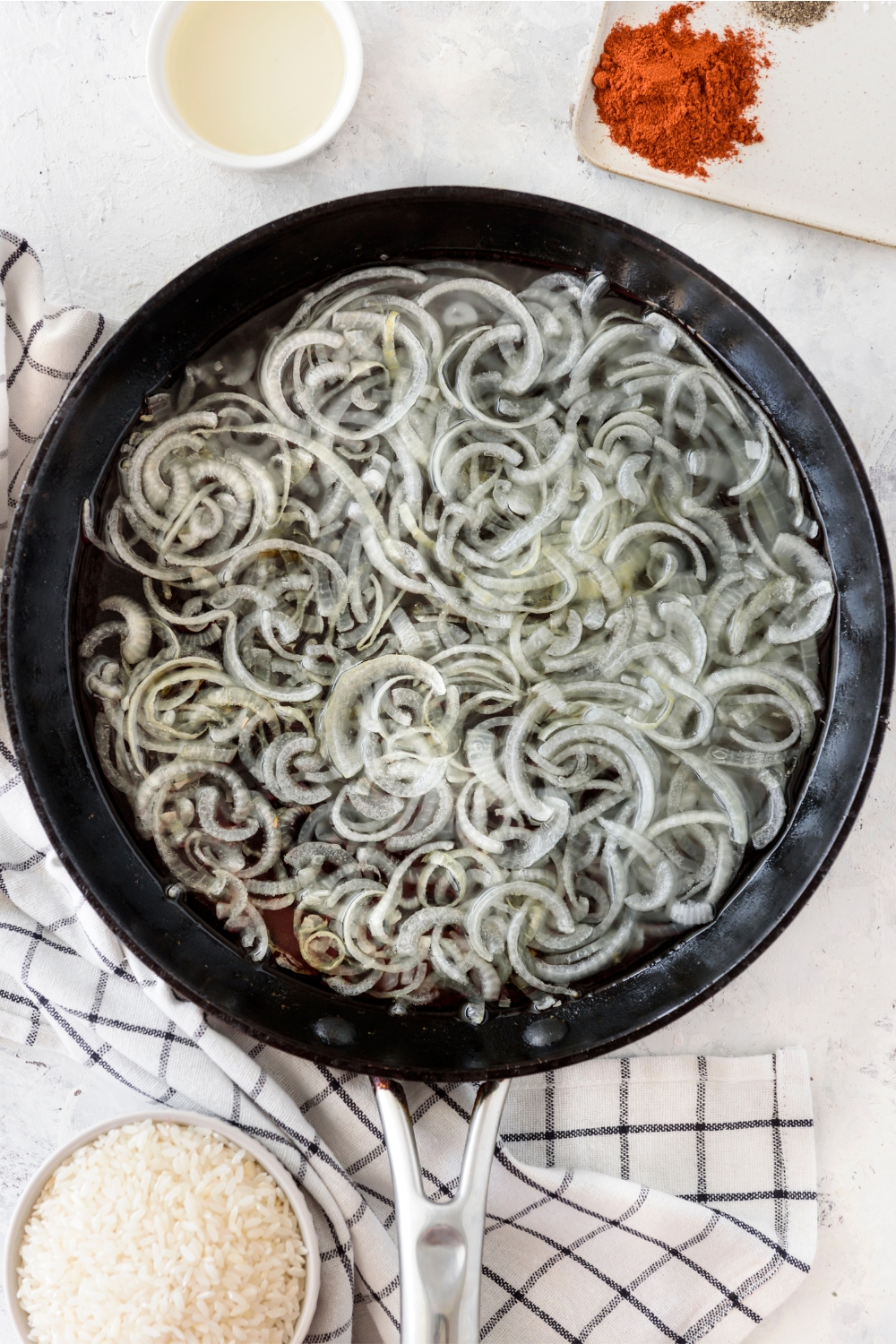 A skillet with sliced onions cooking in oil.