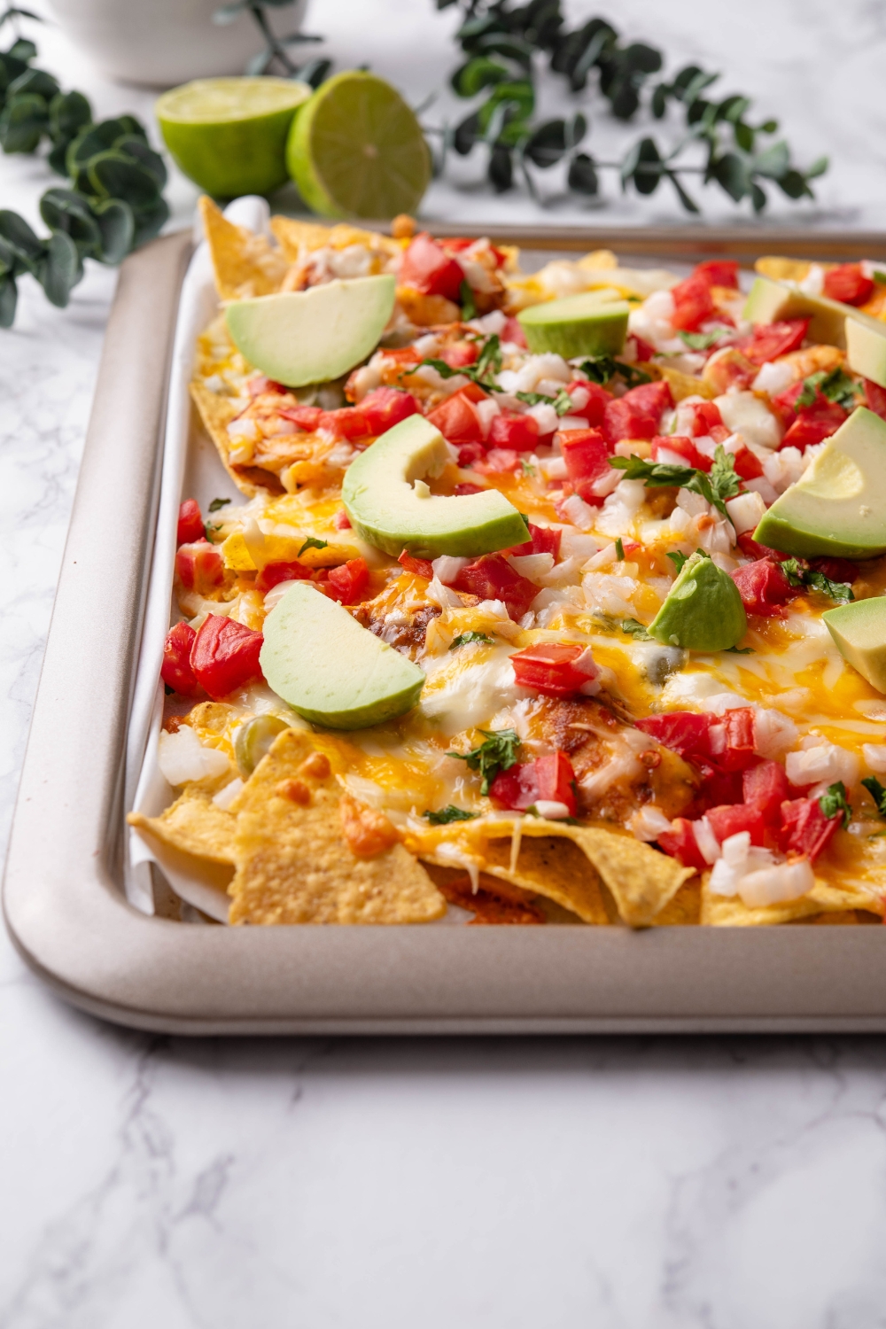 A baking sheet lined with parchment paper topped with seasoned chicken, melted cheese, pico de gallo, and sliced avocado.