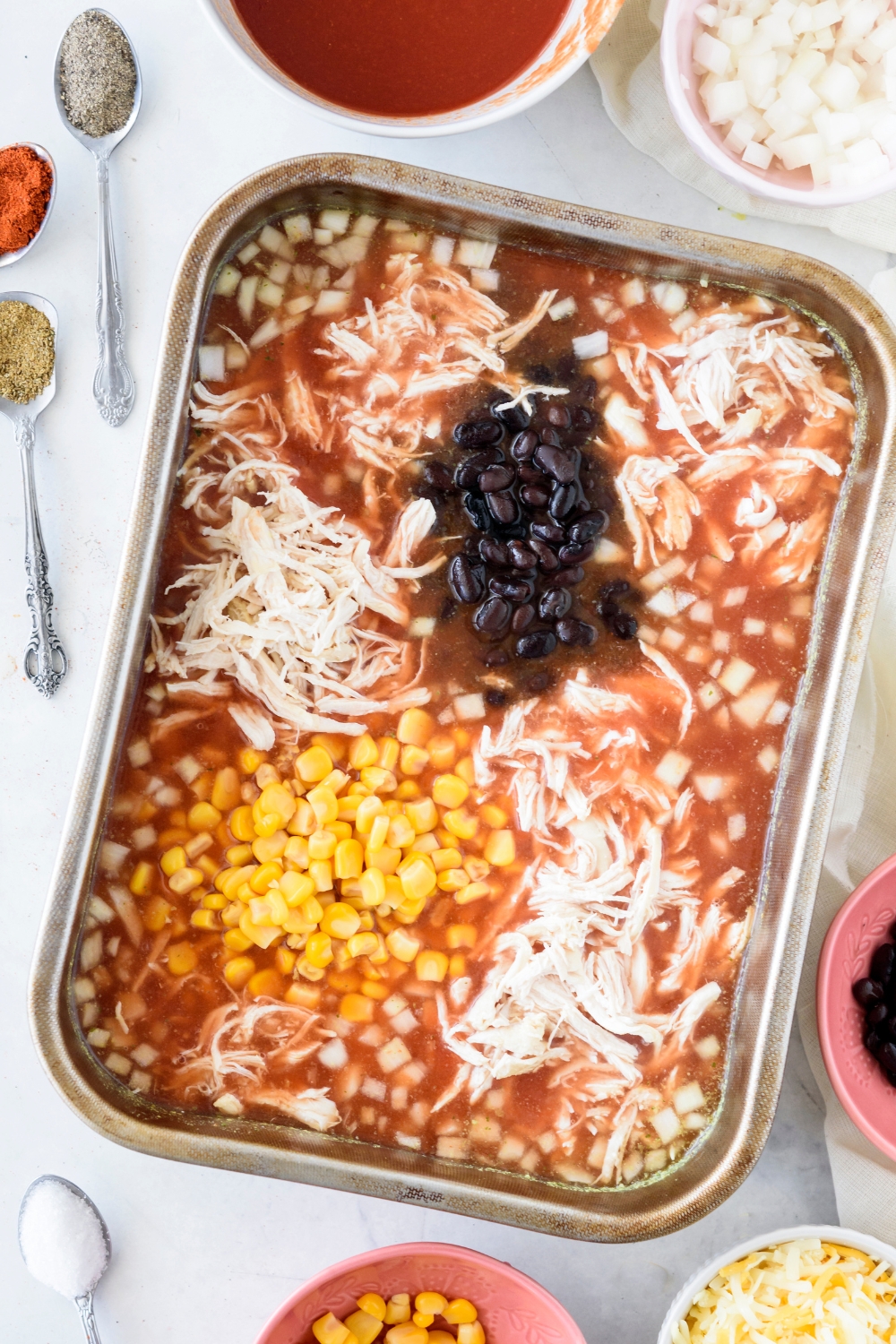 A baking dish filled with shredded chicken, black beans, onion, and corn swimming in a seasoned sauce.