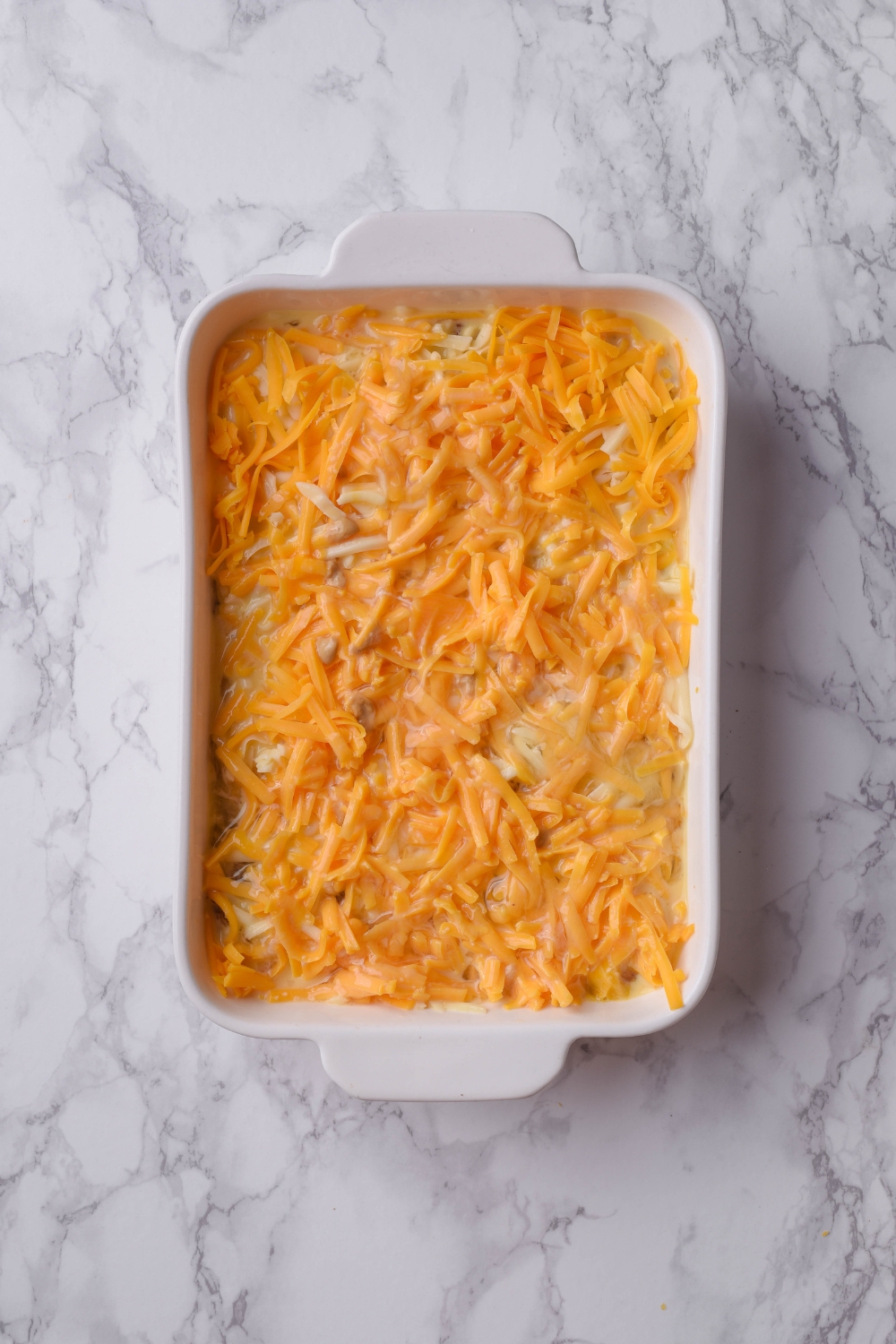 A baking dish filled with casserole covered in shredded cheese.