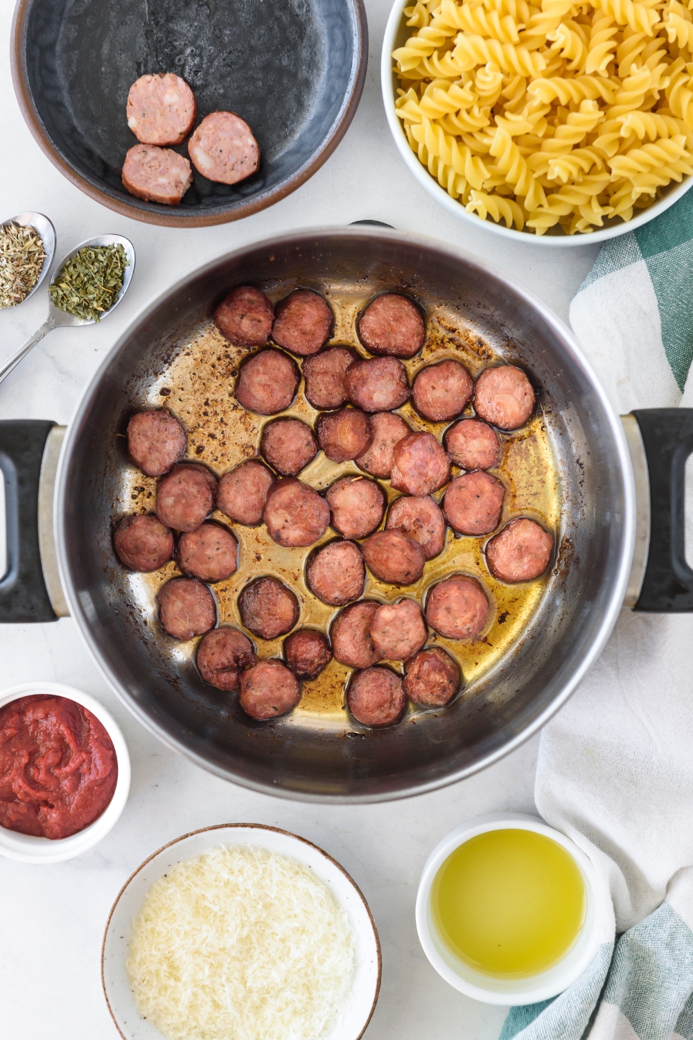 A pot with sausage slices cooking in it. The pot is surrounded by an assortment of ingredients.