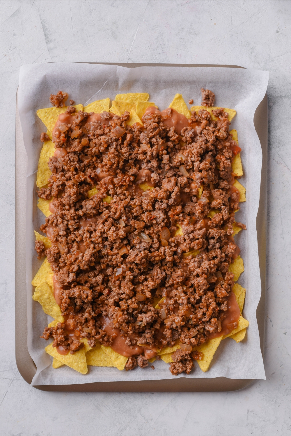 A baking sheet lined with parchment paper topped with tortilla chips and cooked ground beef.