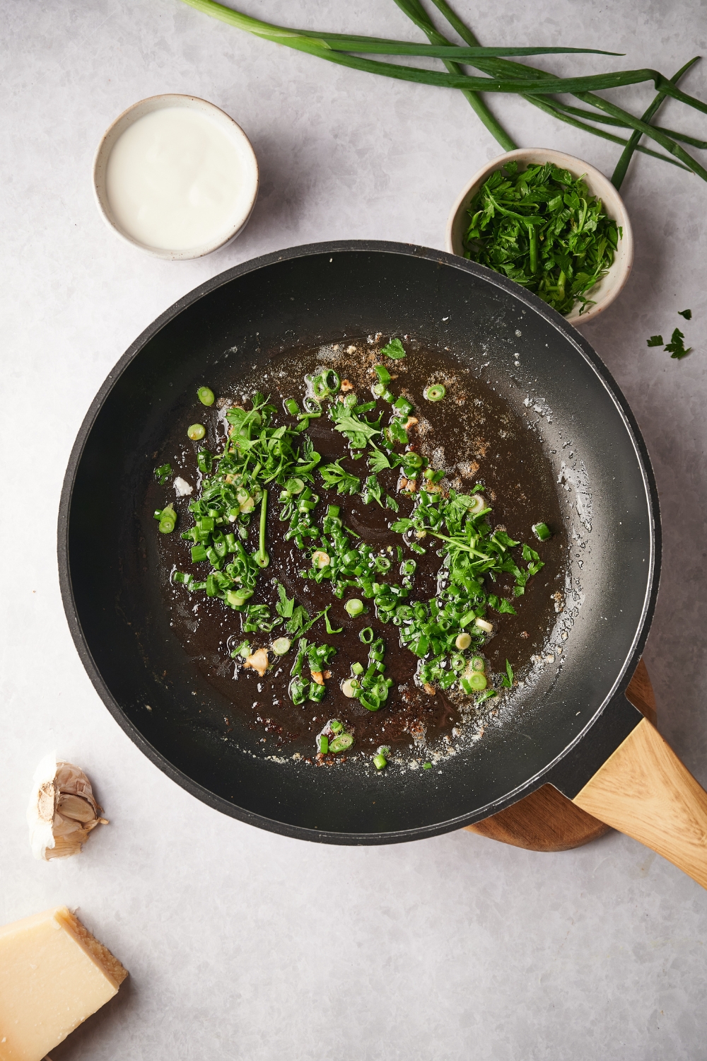 A skillet with fresh herbs, garlic, and green onion cooking in it.