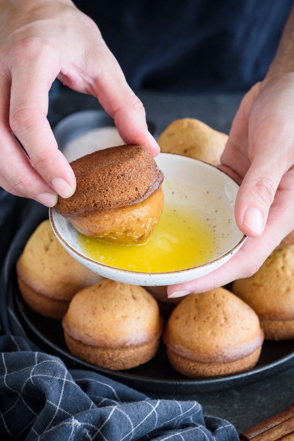 A muffin being dunked in a bowl of melted butter.