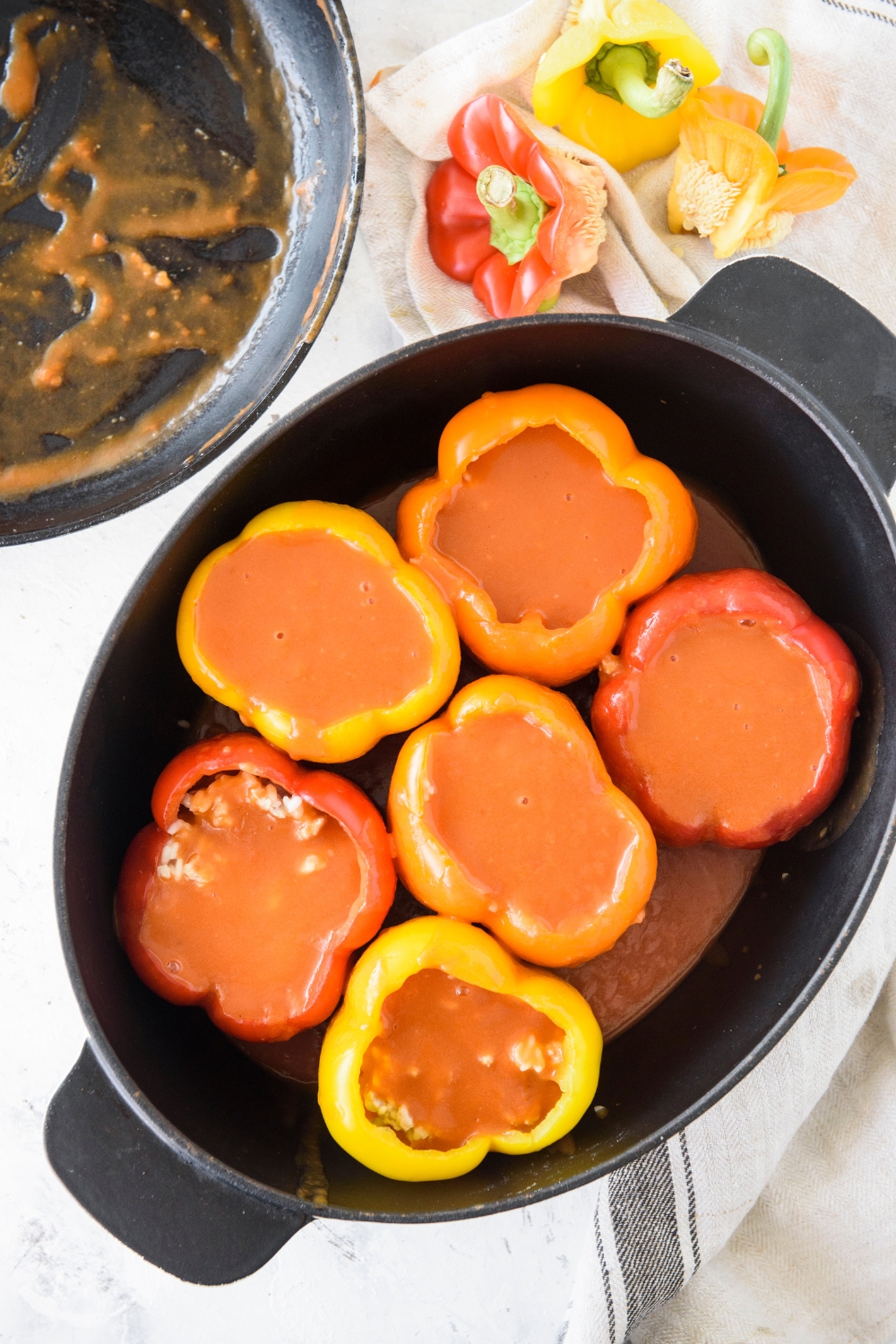 A baking dish filled with bell peppers that have been stuffed with ground meat and rice and each pepper has been topped with tomato sauce.