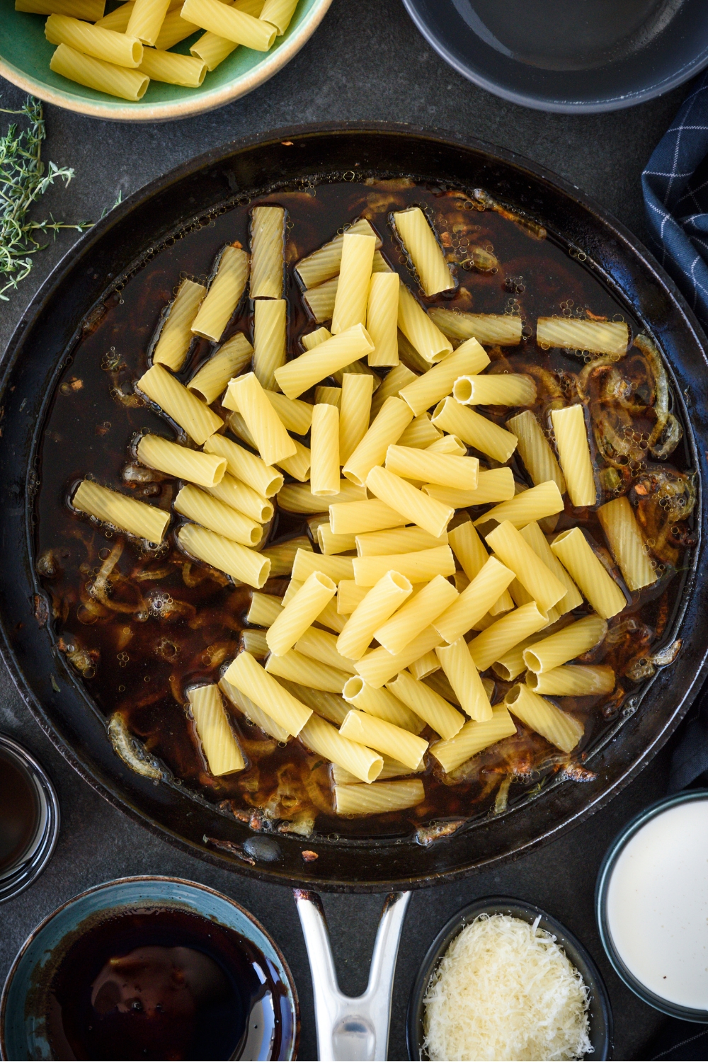 A skillet filled with caramelized onion, broth, and dried pasta.