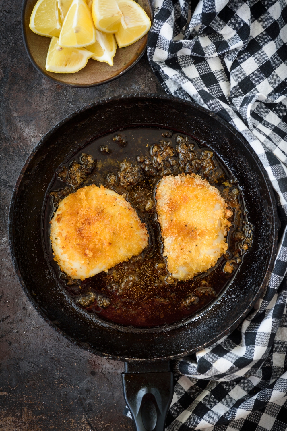 A skillet with two breaded calamari steaks frying in the skillet.