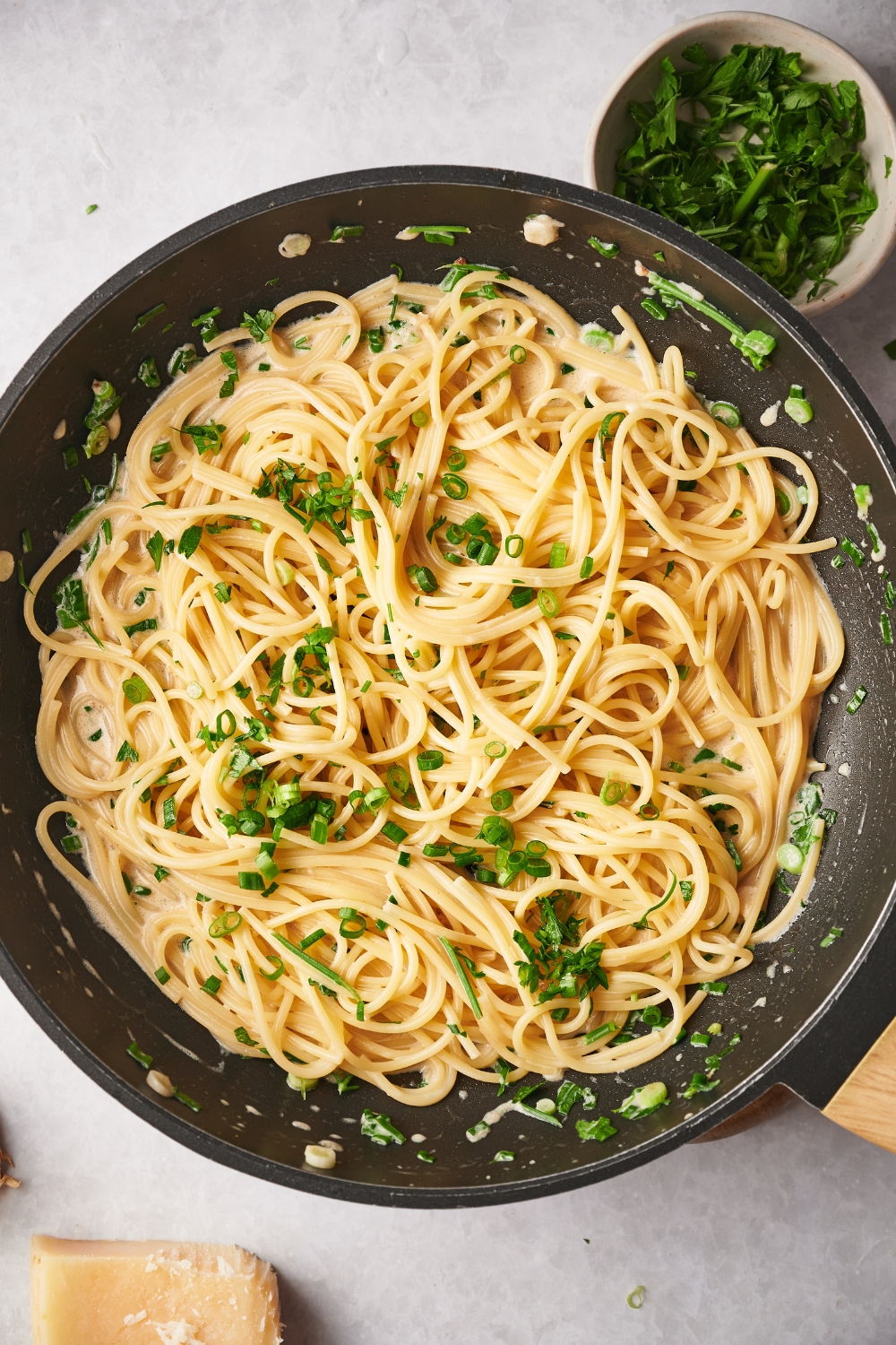 A skillet with cooked spaghetti in a cream sauce and garnished with fresh herbs and green onion.
