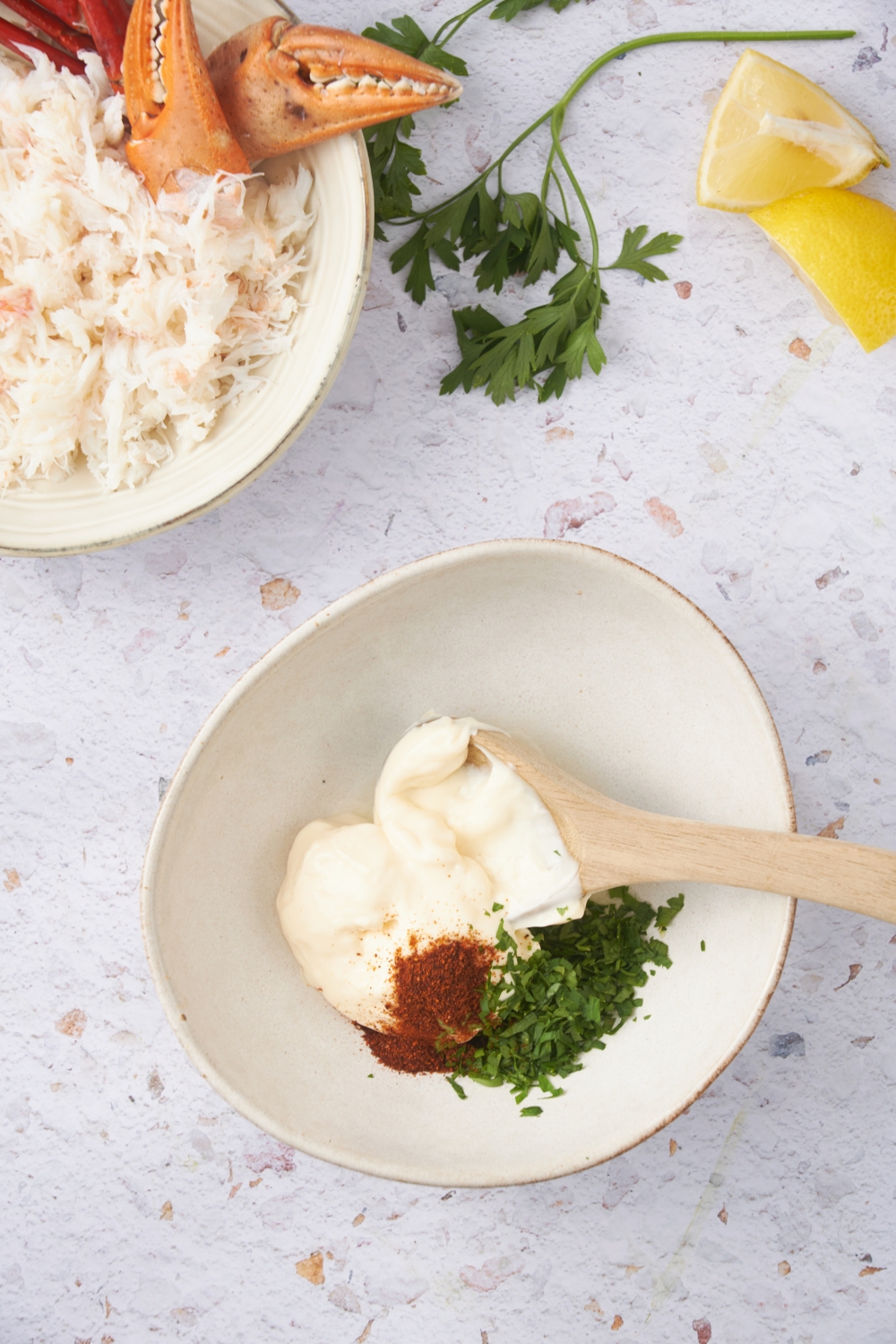 A bowl filled with mayonnaise, spices, and fresh herbs. There is a wooden spoon in the bowl.