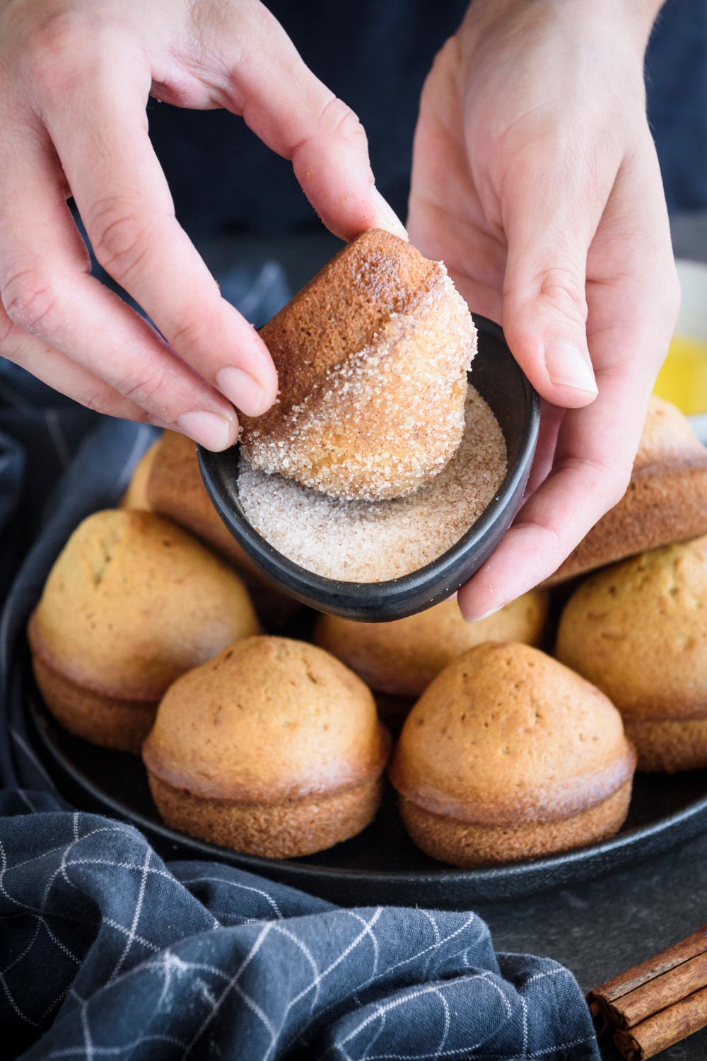 A muffin being dipped in a bowl of cinnamon sugar.