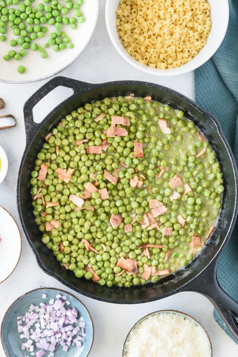 peas, bacon, and shallots boiling in a black skillet