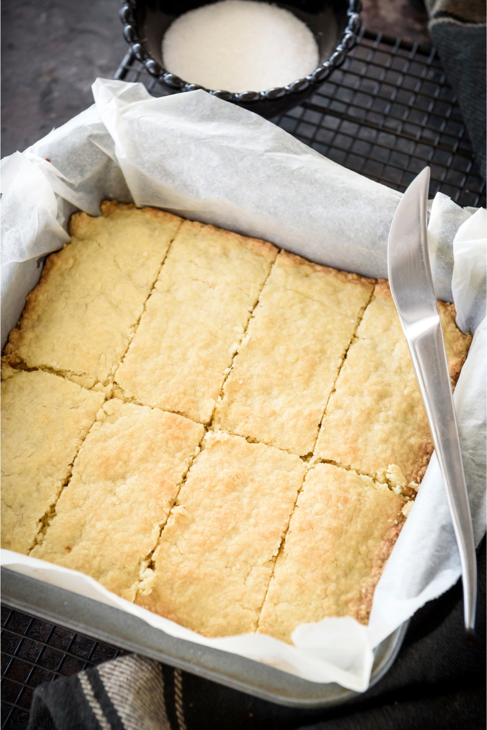 A square baking dish lined with parchment paper with freshly baked biscuits that have been cut into rectangles using a knife.