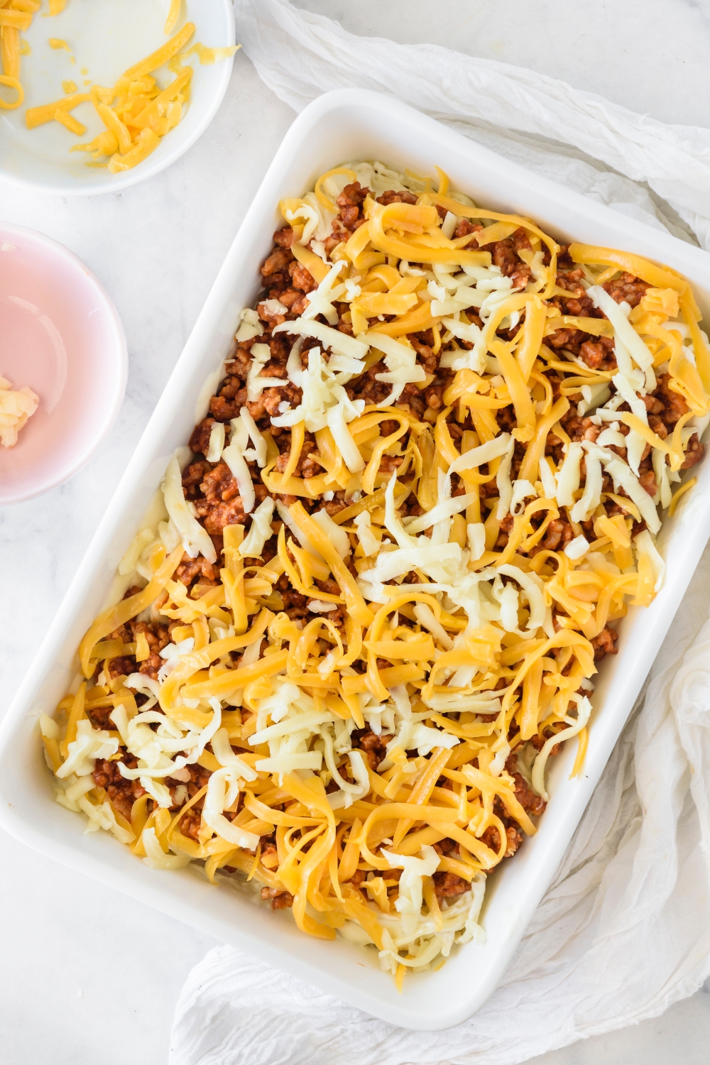 A baking dish filled with cooked spaghetti, seasoned ground meat, and shredded cheese.