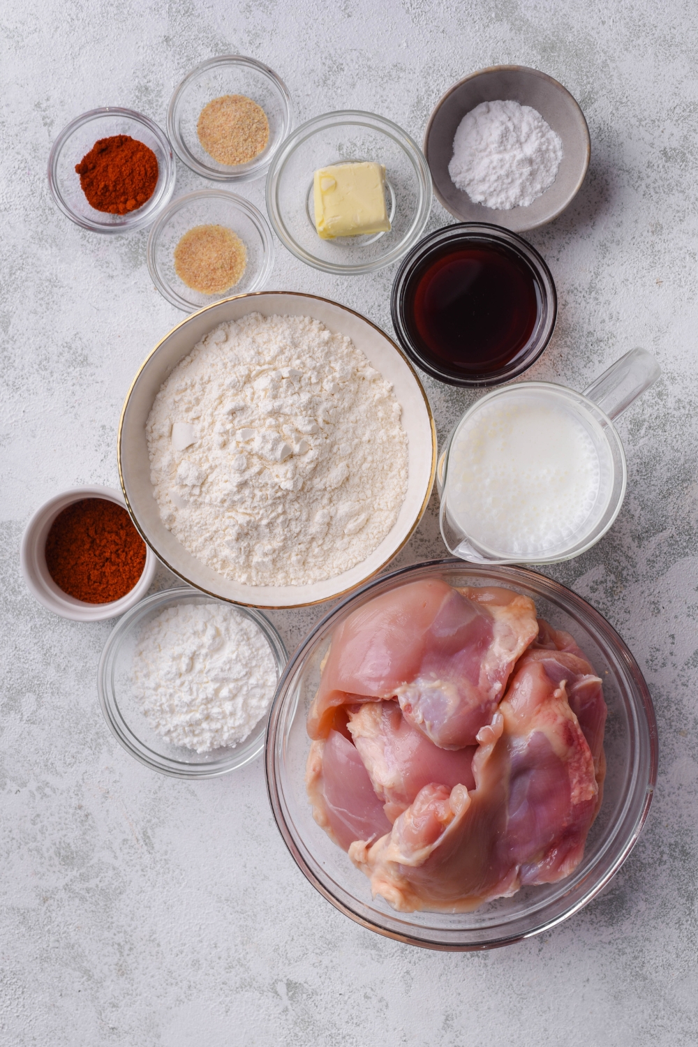 Overhead view of an assortment of ingredients including bowls of raw chicken, flour, chili powder, butter, buttermilk, and seasonings.