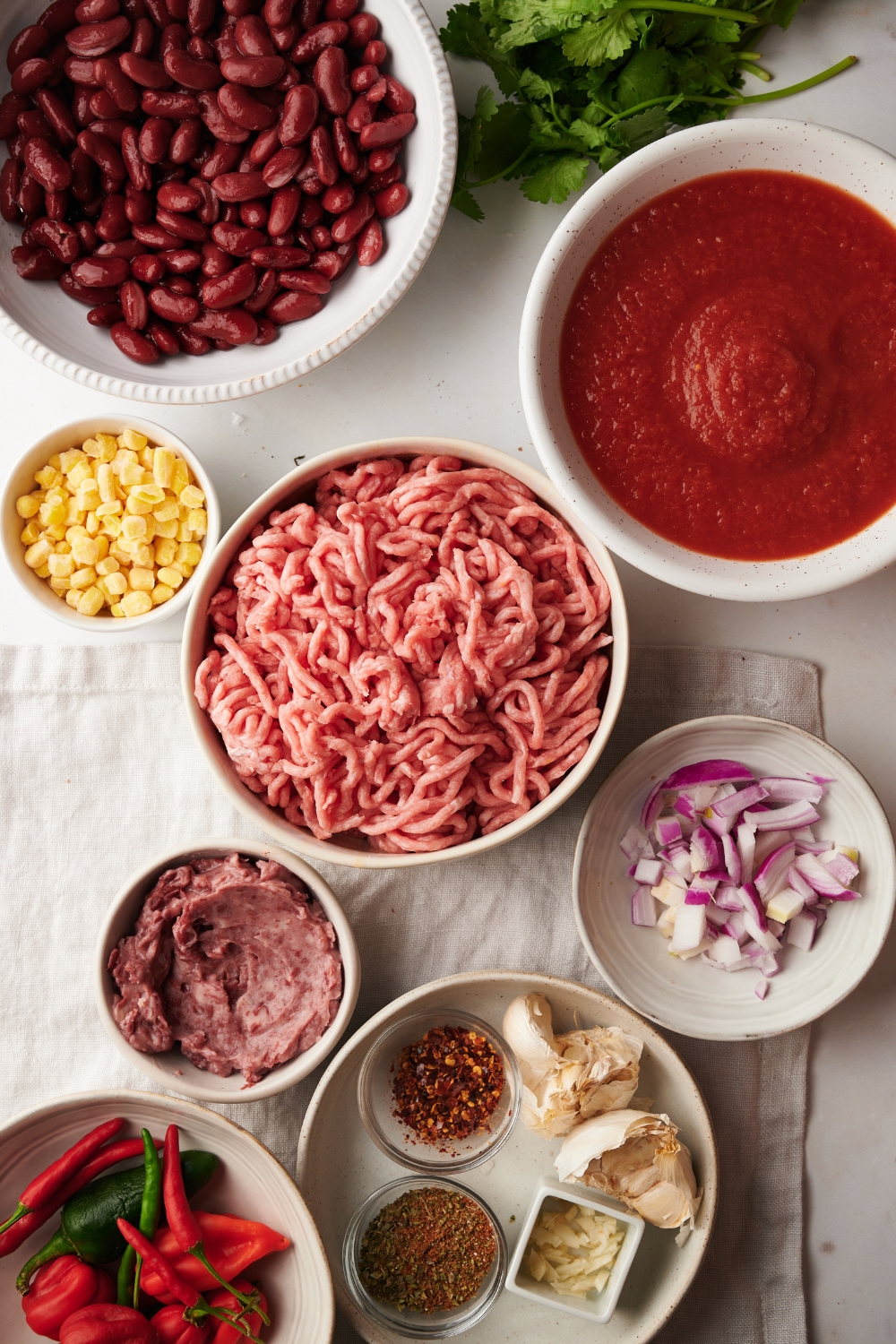 ground meat, tomato sauce, onions, peppers, and spices in separate bowls on a white counter