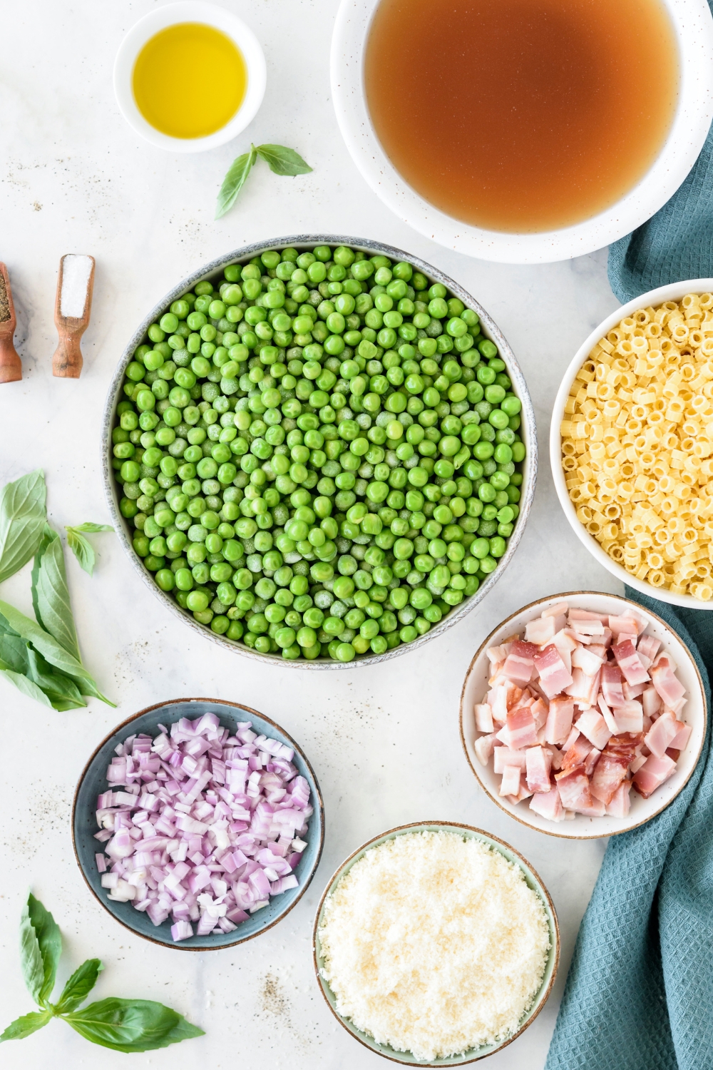 peas, shallots, bacon, and dry pasta in separate bowls on a white counter