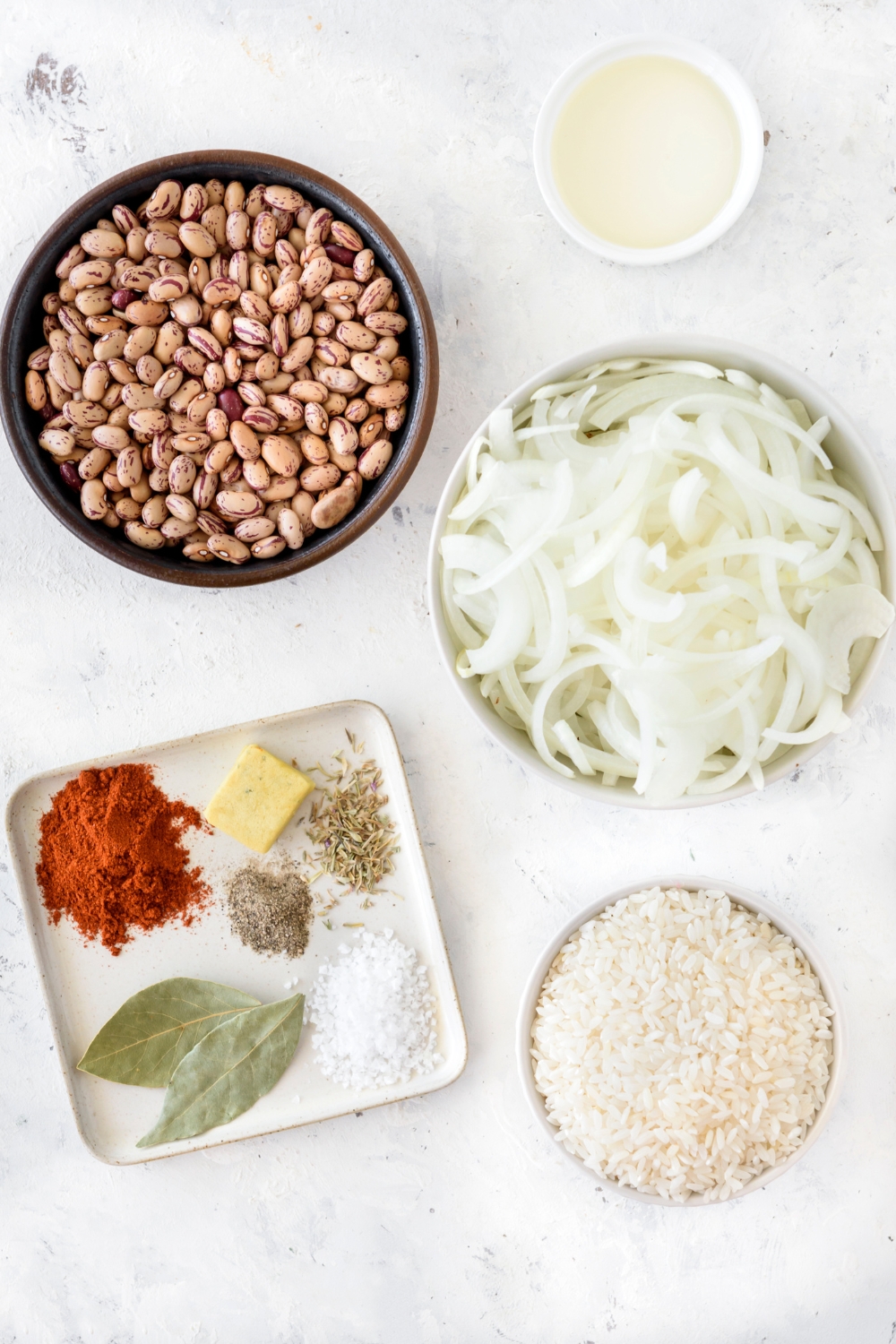 An assortment of ingredients including bowls of pinto beans, sliced onions, dried rice, and a plate of seasonings.