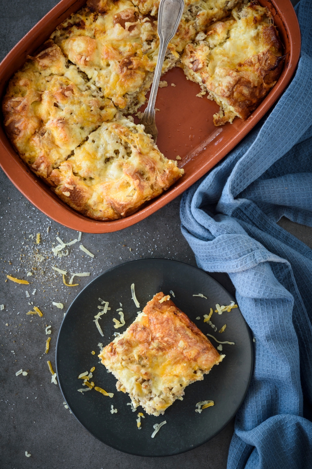 A serving of breakfast casserole on a plate next to a baking dish filled with more casserole.