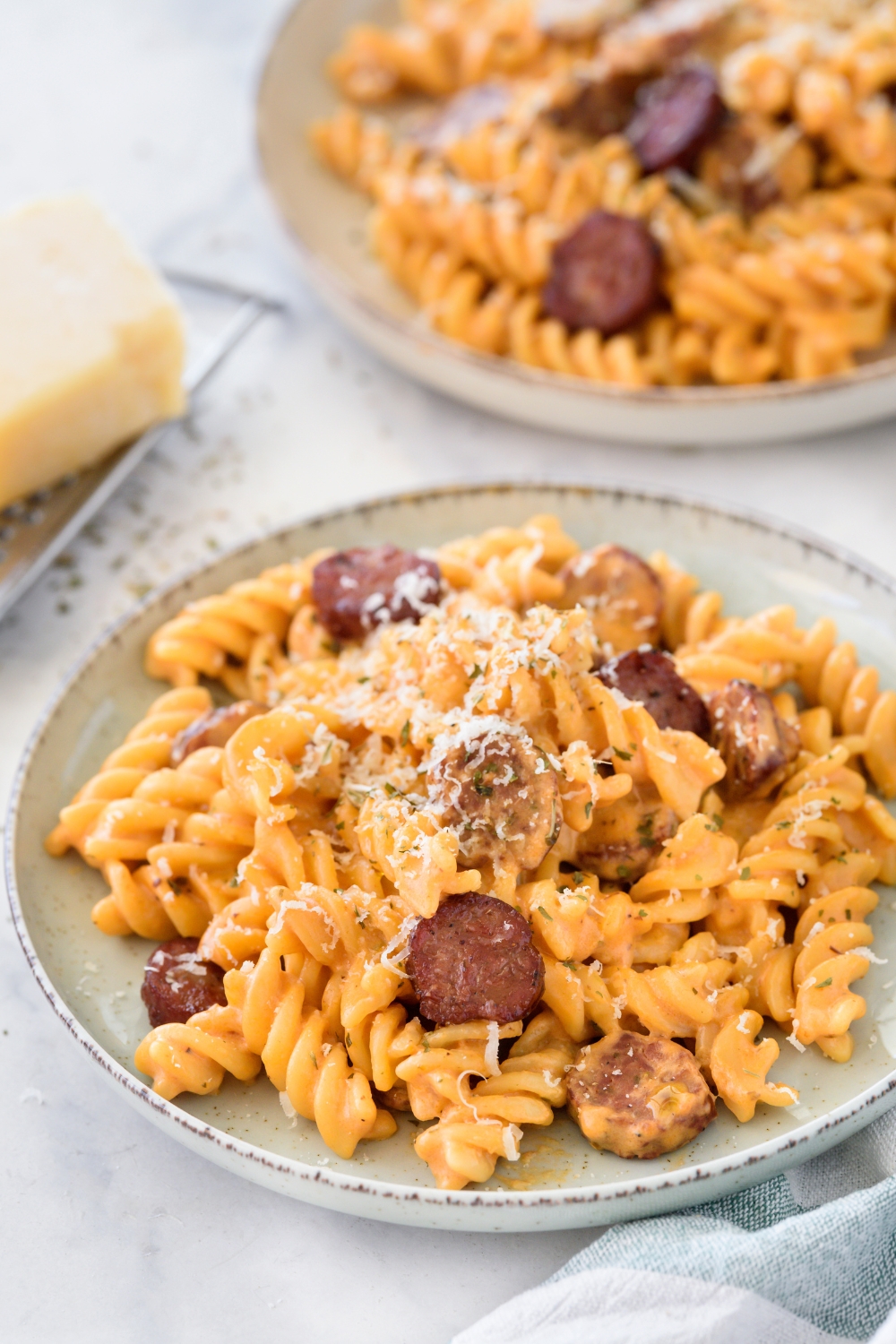 A plate of pasta covered in creamy red sauce with sausage slices mixed in the pasta and cheese on top.
