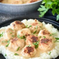 A plate of meatballs covered in fresh herbs and creamy gravy on a bed of rice.