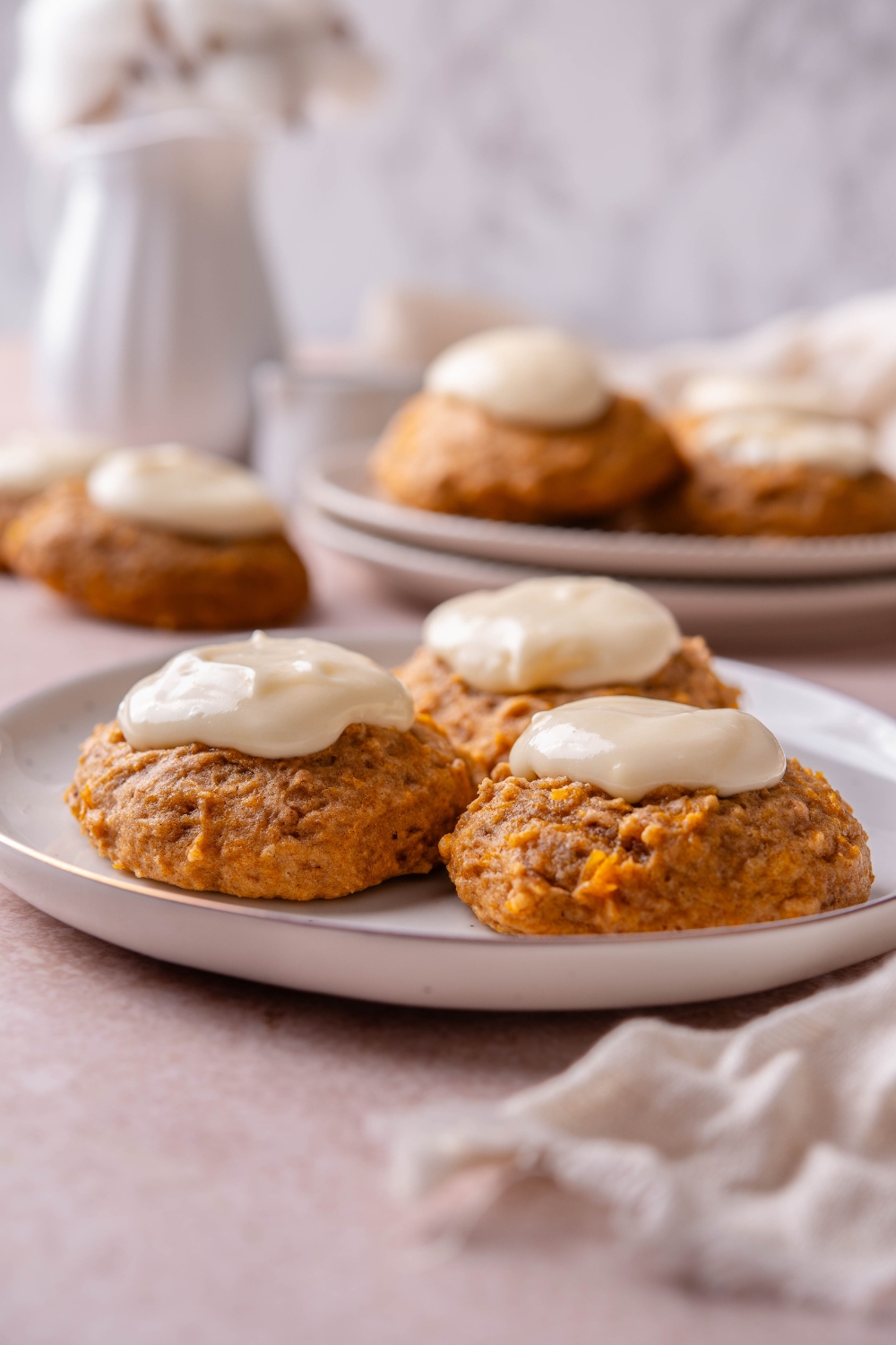 Three pumpkin cookies on a plate and topped with a dollop of white frosting.