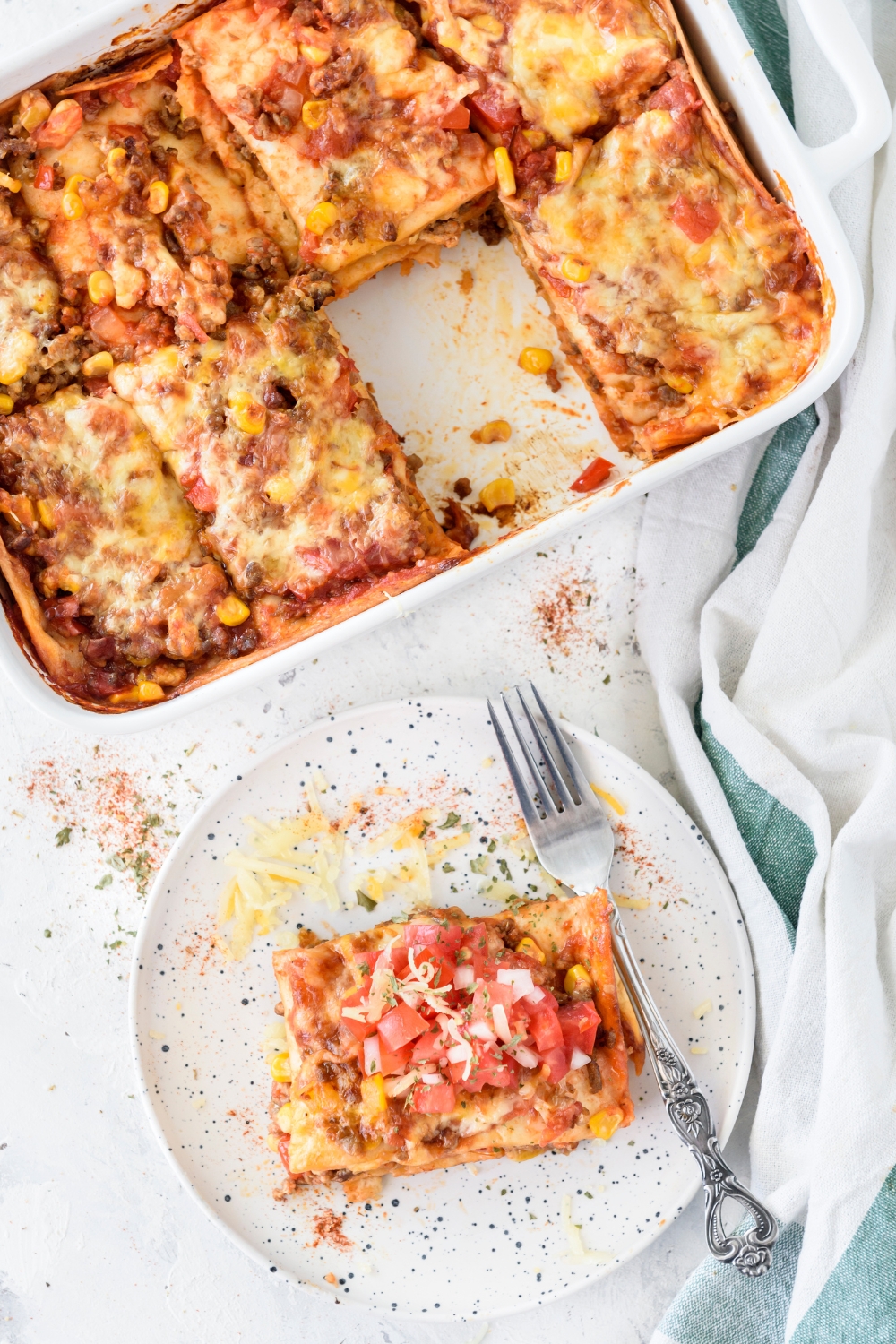 A square serving of casserole topped with melted cheese and salsa next to a baking dish filled with more casserole.